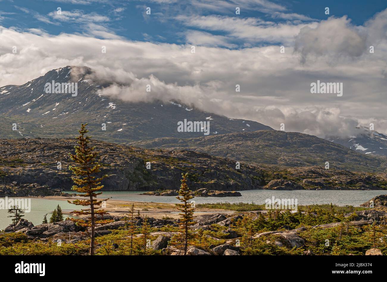 Skagway, Alaska, USA - 20. Juli 2011: Klondike Highway nach Kanada. Schwere Wolkenlandschaft über den kanadischen Rockies mit Schneepatches und Summer Lake unten. Stockfoto