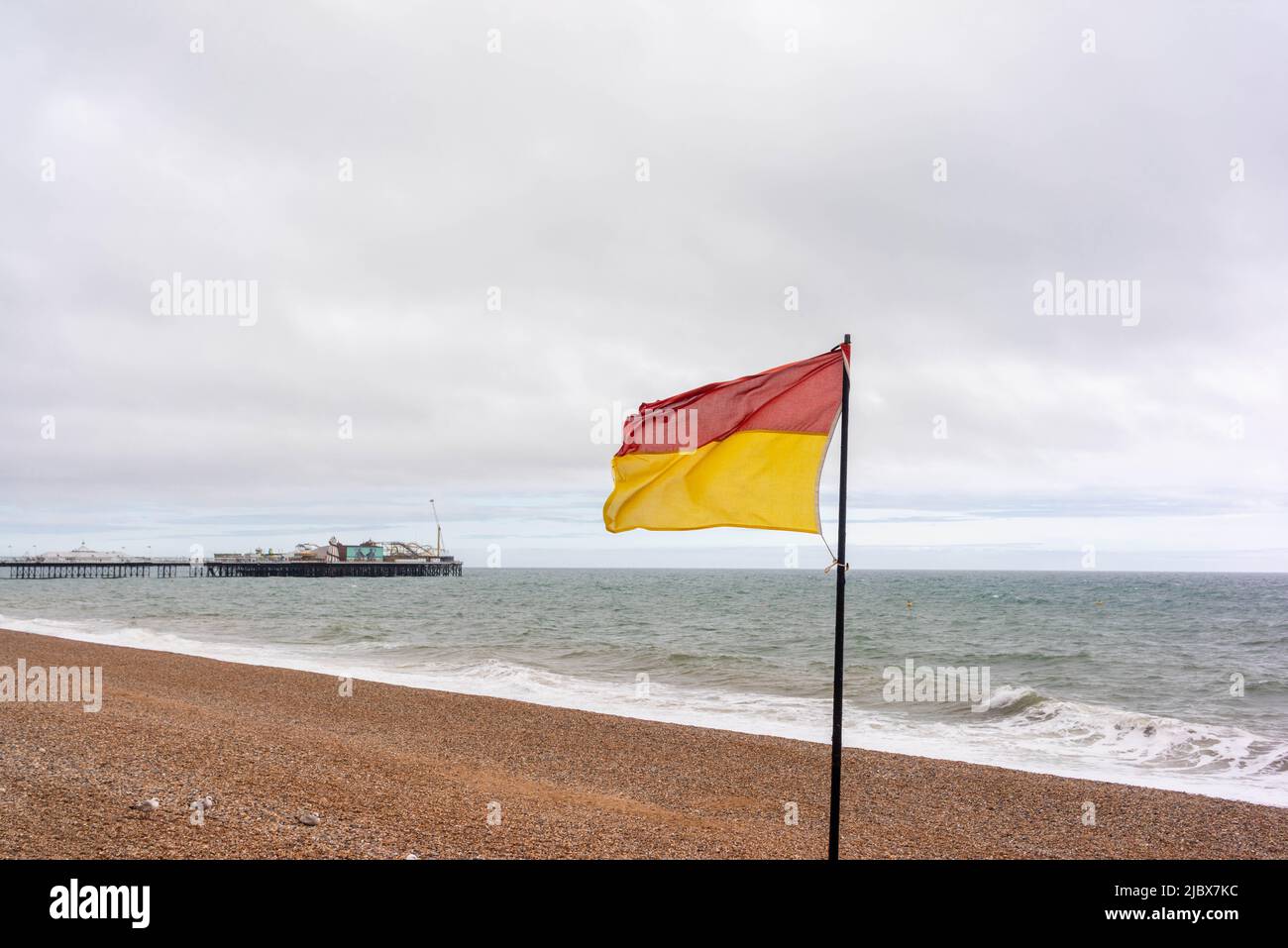 Rote und gelbe Rettungsschwimmer mit Dienstflagge am Brighton Beach mit dem Brighton Pier im Hintergrund an einem bewölkten Tag, East Sussex, England, Großbritannien Stockfoto