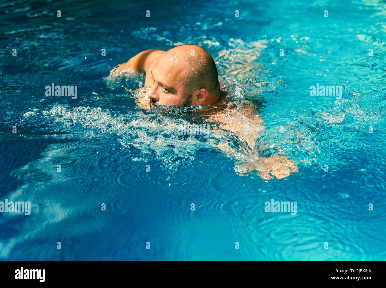 Großer Mann, der im Pool mit blauem Wasser schwimmte. Sportliche Aktivitäten zur Gesundheit und Prävention von Krankheiten im Zusammenhang mit Fettleibigkeit. Stockfoto