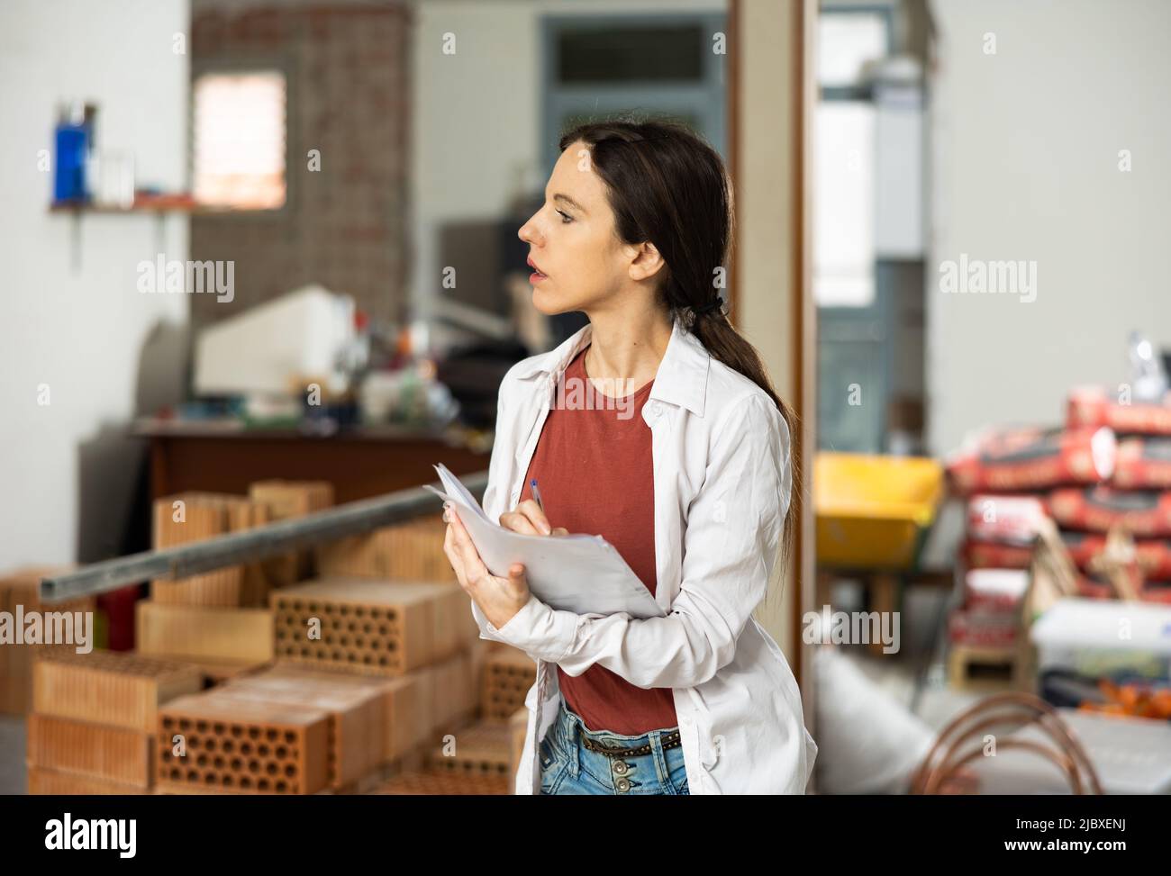 Designerin mit Papieren, die in der Wohnung arbeiten, die gerade renoviert wird Stockfoto