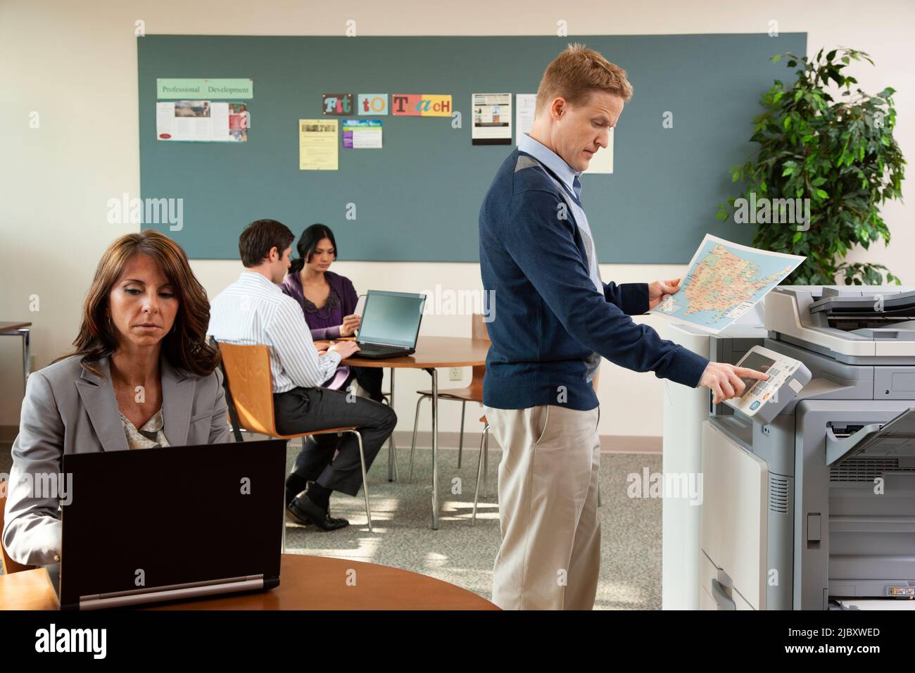 Geschäftsleute, die im Büro an Laptops und Kopierern arbeiten. Stockfoto