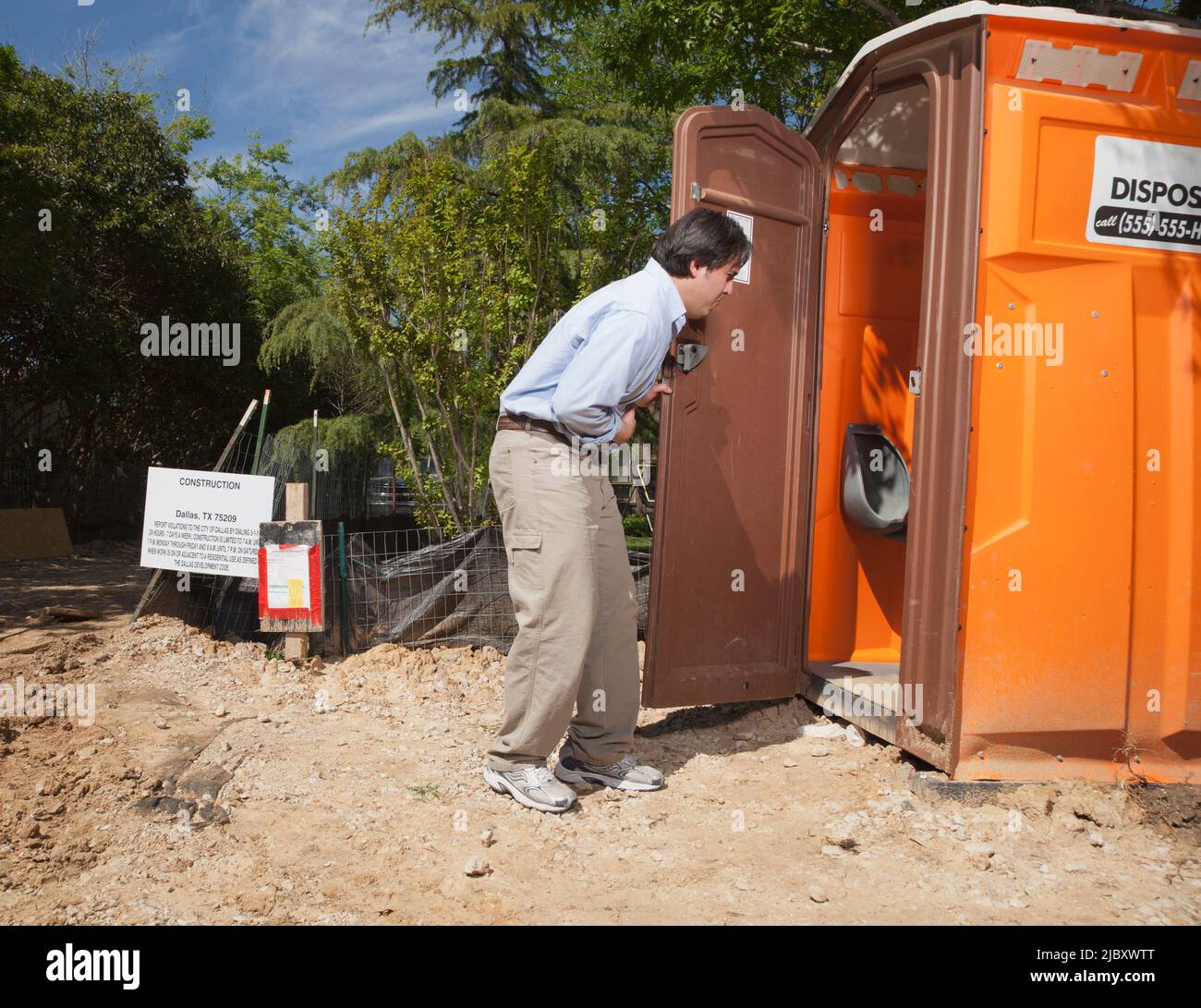 Mann, der seinen Magen hielt, während er auf einer Wohnbaustelle eine tragbare Toilette betrat Stockfoto