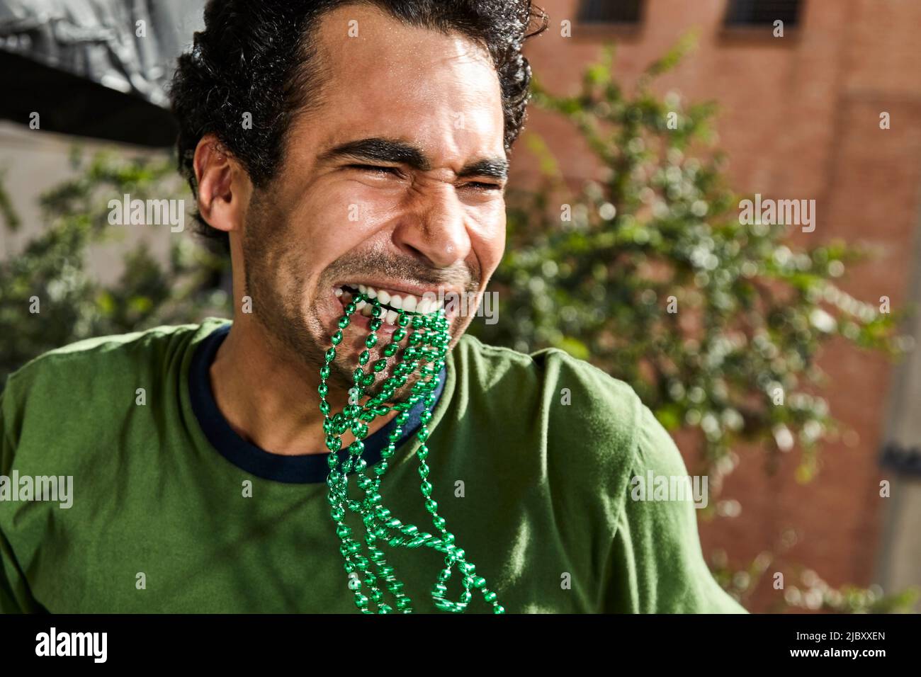 Fröhlicher Mann mit grünen St. Patrick's Day Perlen im Mund, der auf einer Party tanzt. Stockfoto