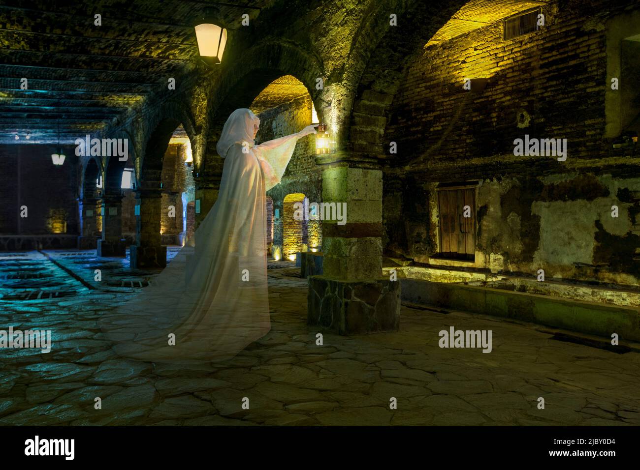 Weiblicher Geist mit Laterne, ganz in Weiß gekleidet und in einem höhlenhaften Steinkeller stehend Stockfoto