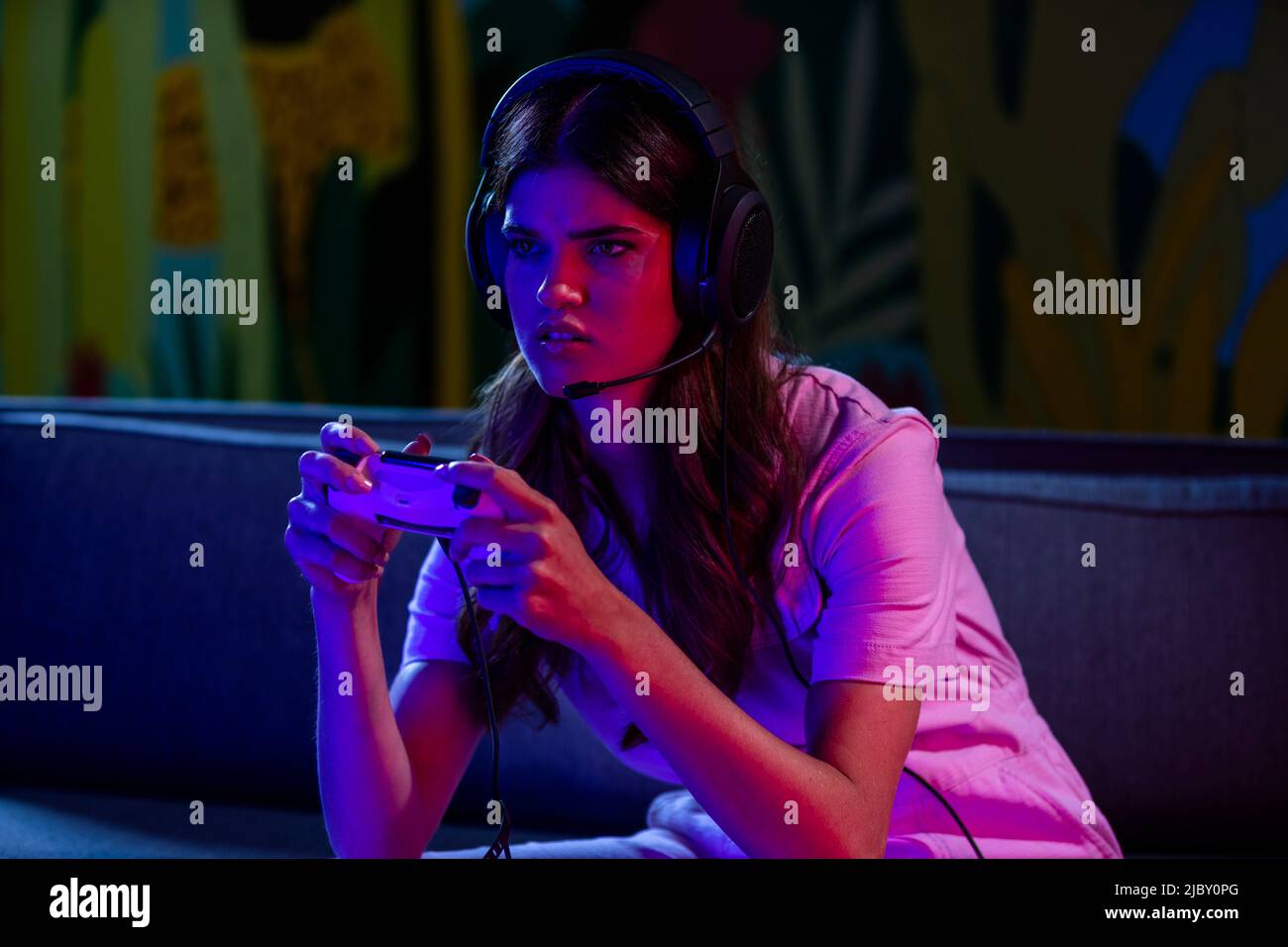Eine wild aussehende junge Frau, die sich nach vorne lehnte und den Game Controller hoch hielt, während sie nachts ein Videospiel spielte. Stockfoto