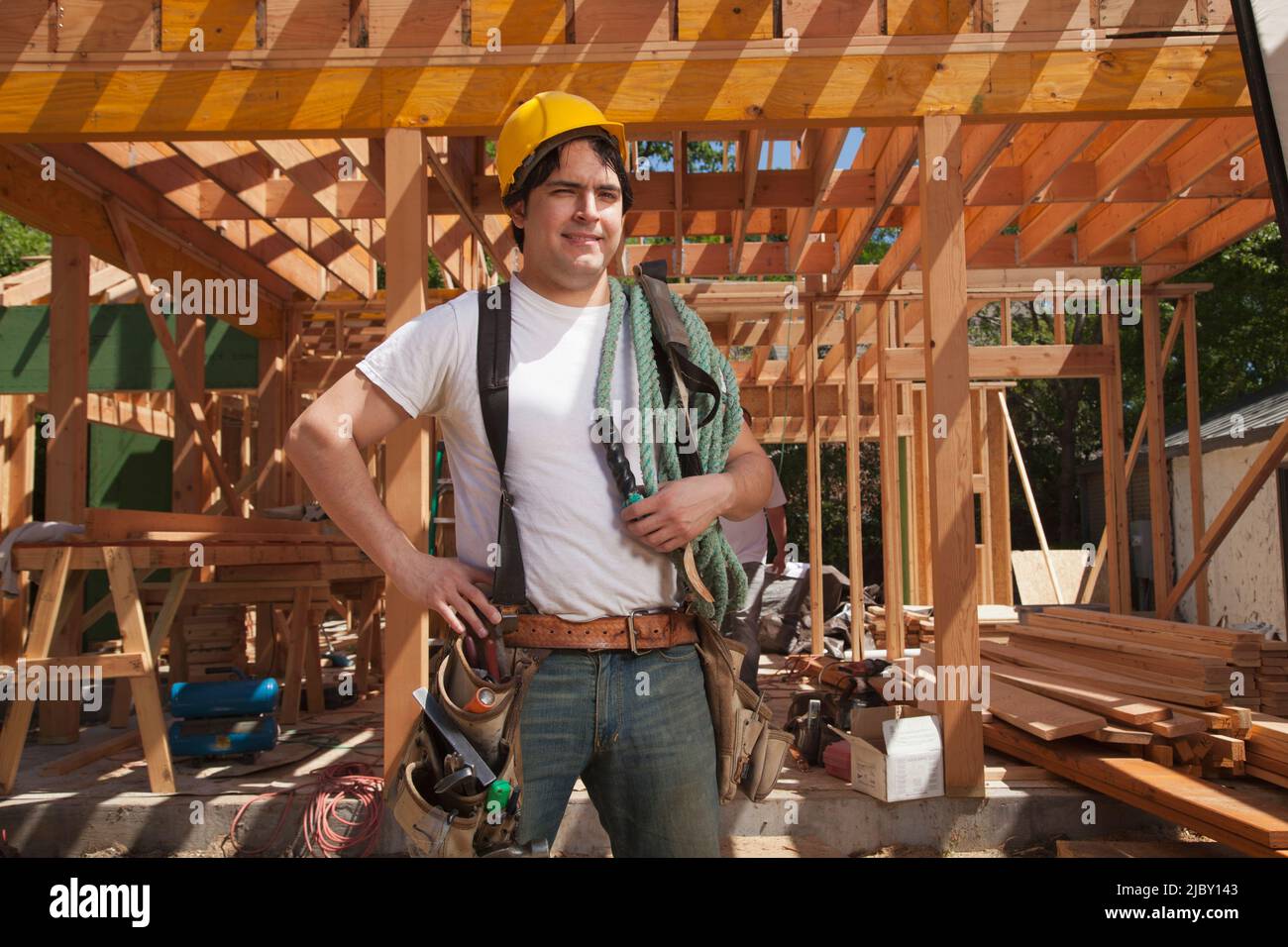 Porträt eines Bauarbeiters, der einen Hut und einen Werkzeuggürtel trägt, während er auf der Baustelle steht Stockfoto
