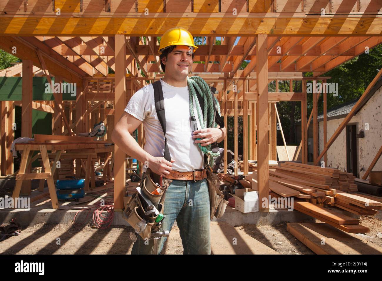 Porträt eines Bauarbeiters, der einen Hut und einen Werkzeuggürtel trägt, während er auf der Baustelle steht Stockfoto