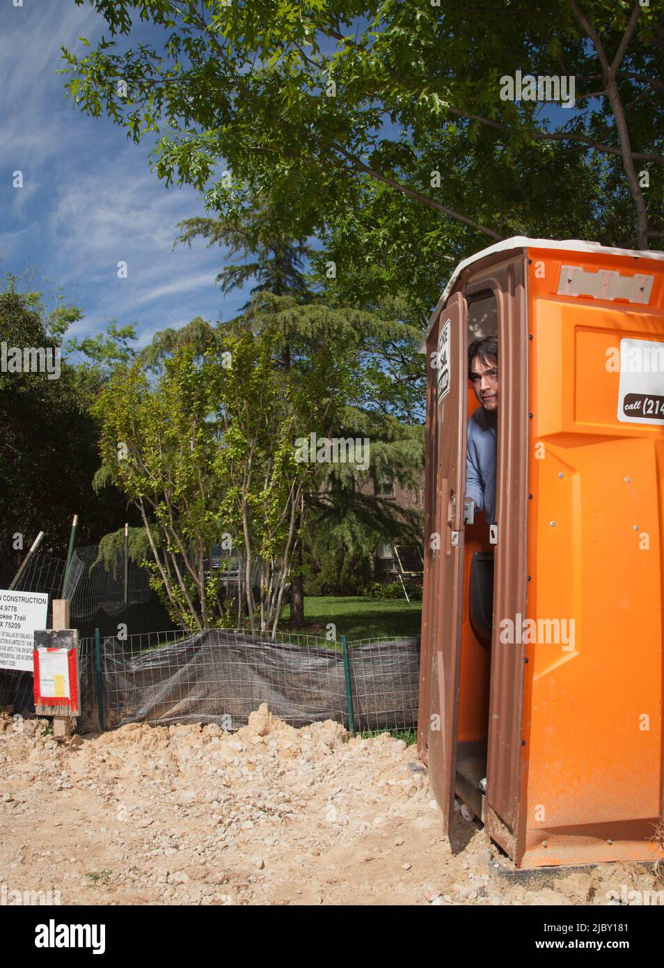 Mann, der auf einer Wohnbaustelle aus der Tür einer tragbaren Toilette schaut Stockfoto