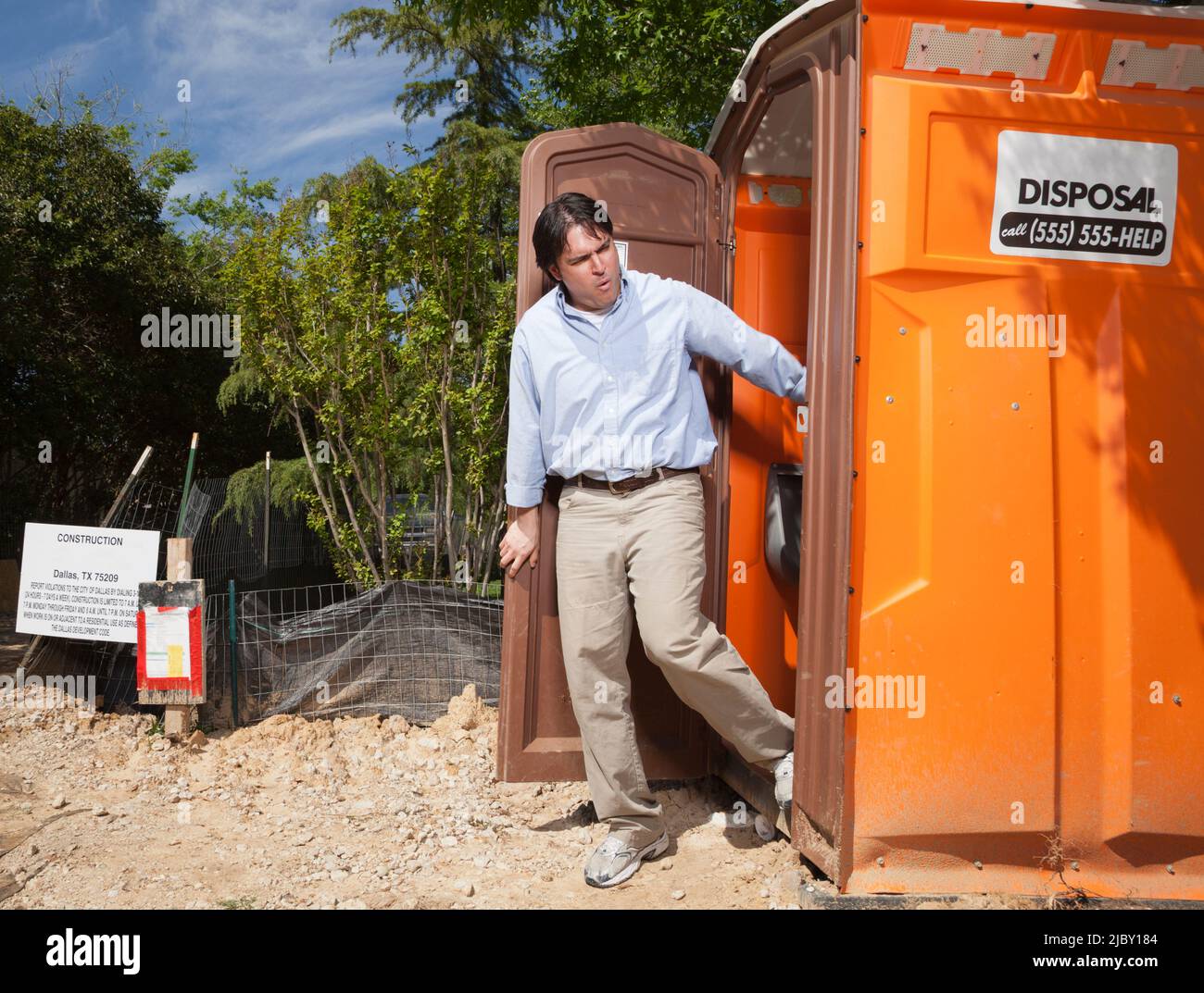 Mann, der aus einer tragbaren Toilette auf einer Wohnbaustelle aus Ekel herauskommt Stockfoto