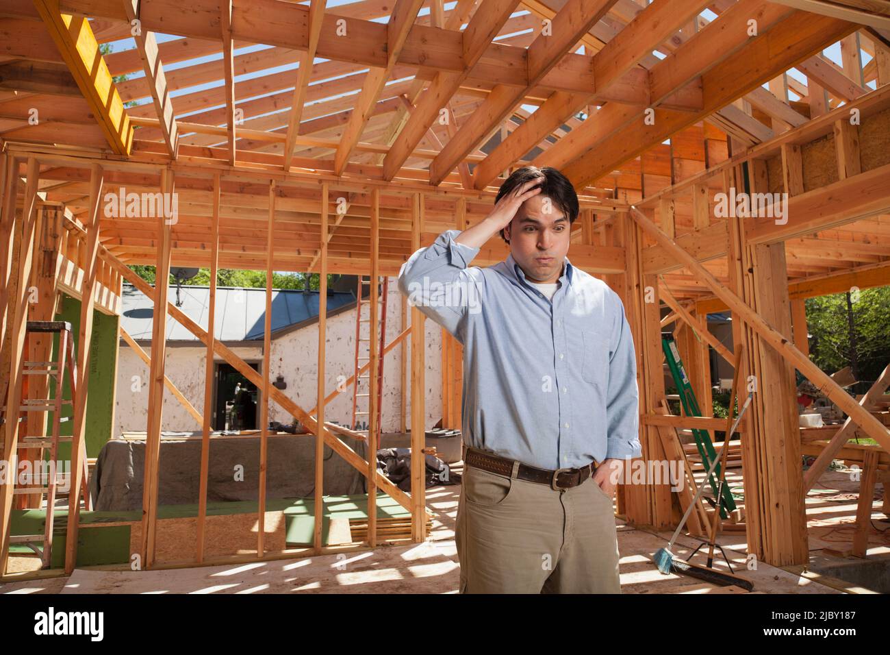 Mann mit der Hand auf dem Kopf und blickte in Sorge auf eine Wohnbaustelle Stockfoto