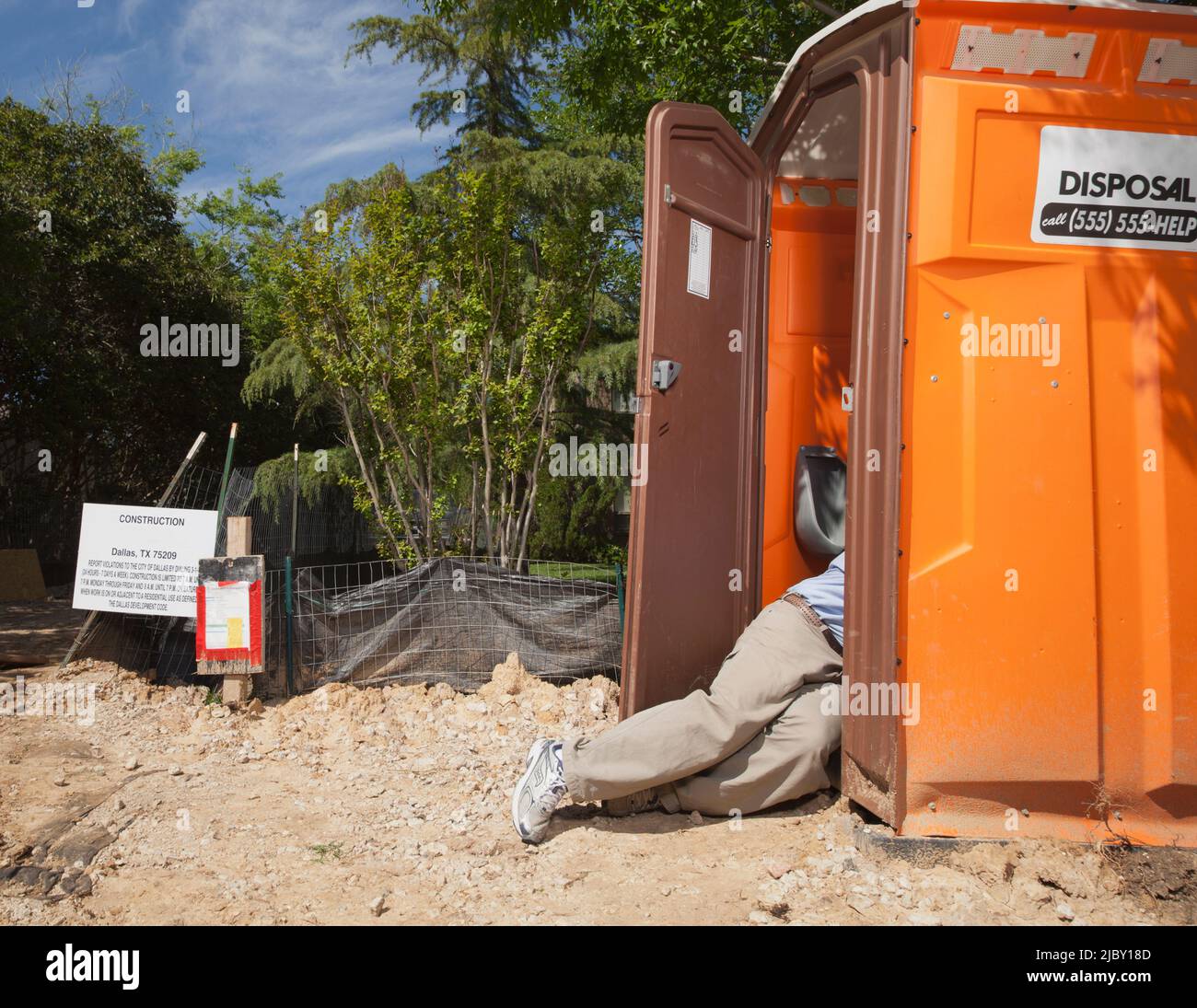 Mann, der halb innen und halb außerhalb einer tragbaren Toilette auf einer Wohnbaustelle liegt Stockfoto