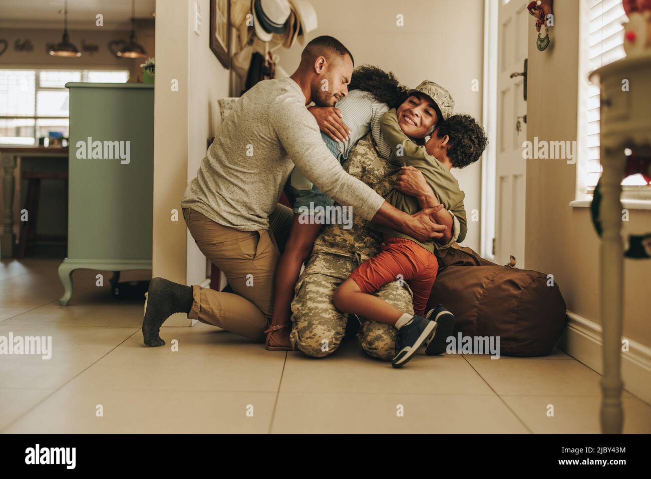 Fröhliche militärische Heimkehr. Die Soldatinnen vereinigen sich nach dem Militärdienst mit ihrem Mann und ihren Kindern. Servicefrau umarmt ihre Familie afte Stockfoto