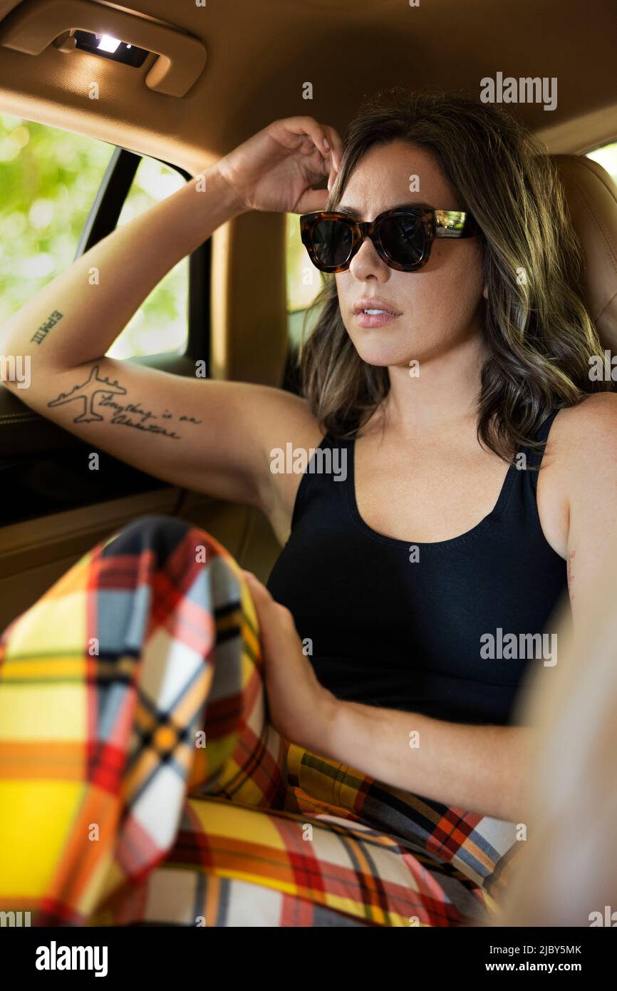 Porträt einer lässig gekleideten Frau in Sonnenbrille mit Tattoos auf dem Rücksitz einer Luxuslimousine Stockfoto