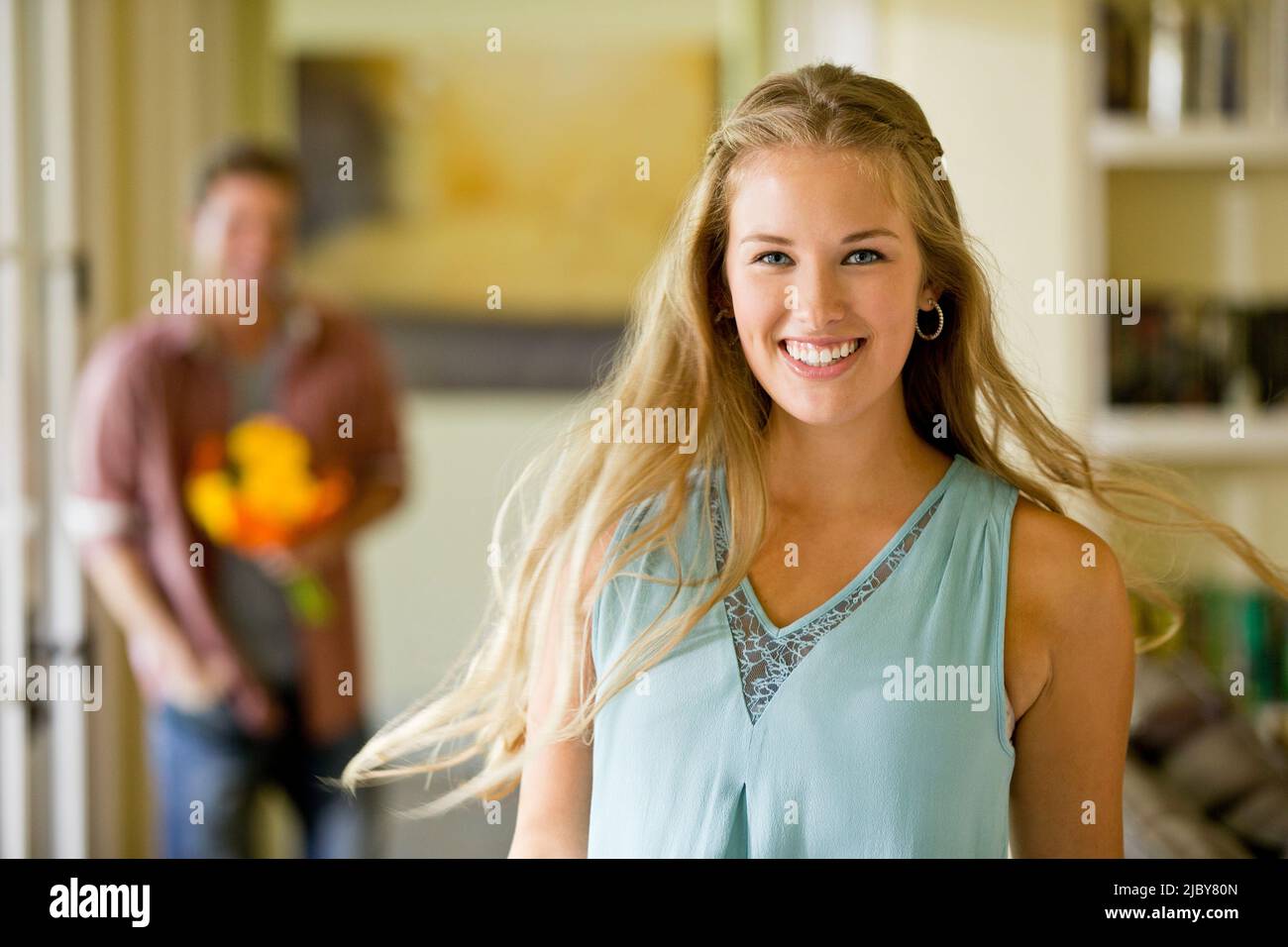 Porträt einer jungen Frau, die sich der Kamera zuwendet, während sie mit einem Blumenstrauß auf ihren Freund zugeht Stockfoto