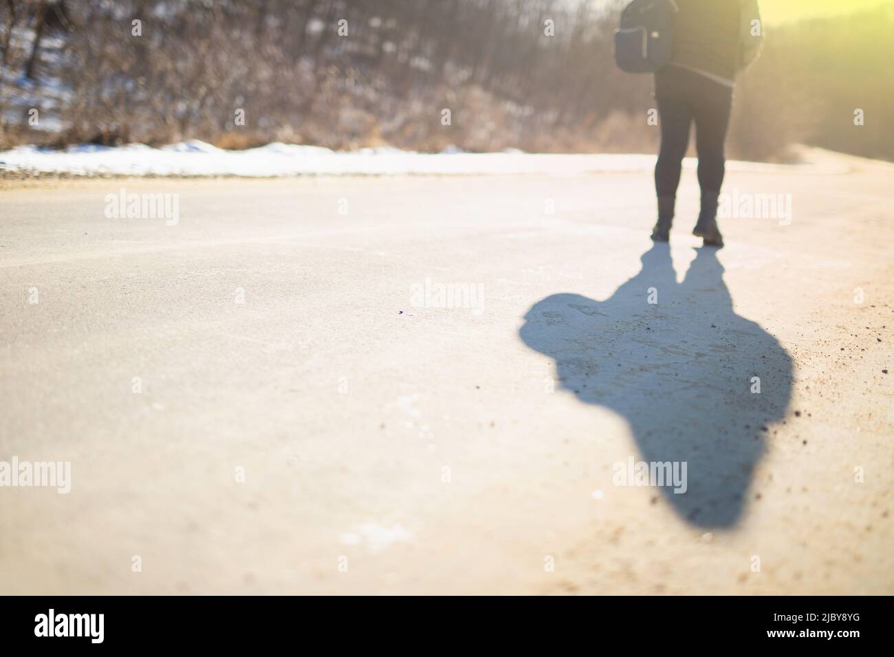 Frau im Winter warme Jacke auf der Straße bei Sonnenuntergang im Winter trägt einen Rucksack auf der Schulter. Stockfoto