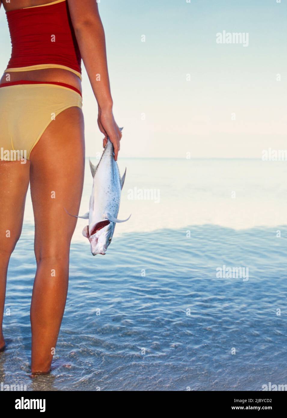 Junge Frau in zweiteiligem Badeanzug, die im tropischen Wasser steht und Fische hält Stockfoto