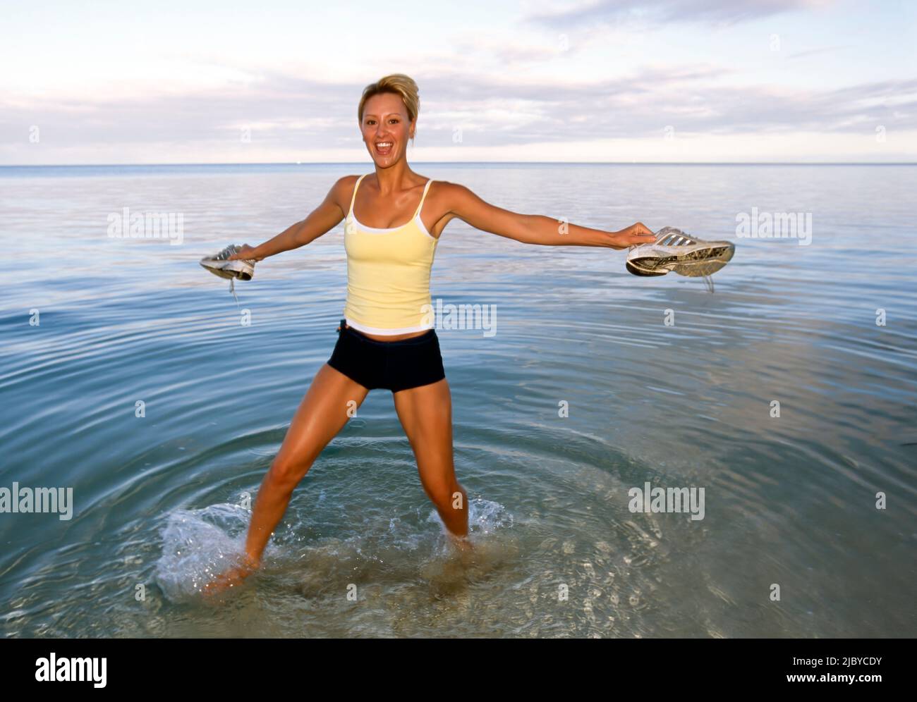 Junge Frau, die am tropischen Strand im Wasser spielt und lächelt Stockfoto