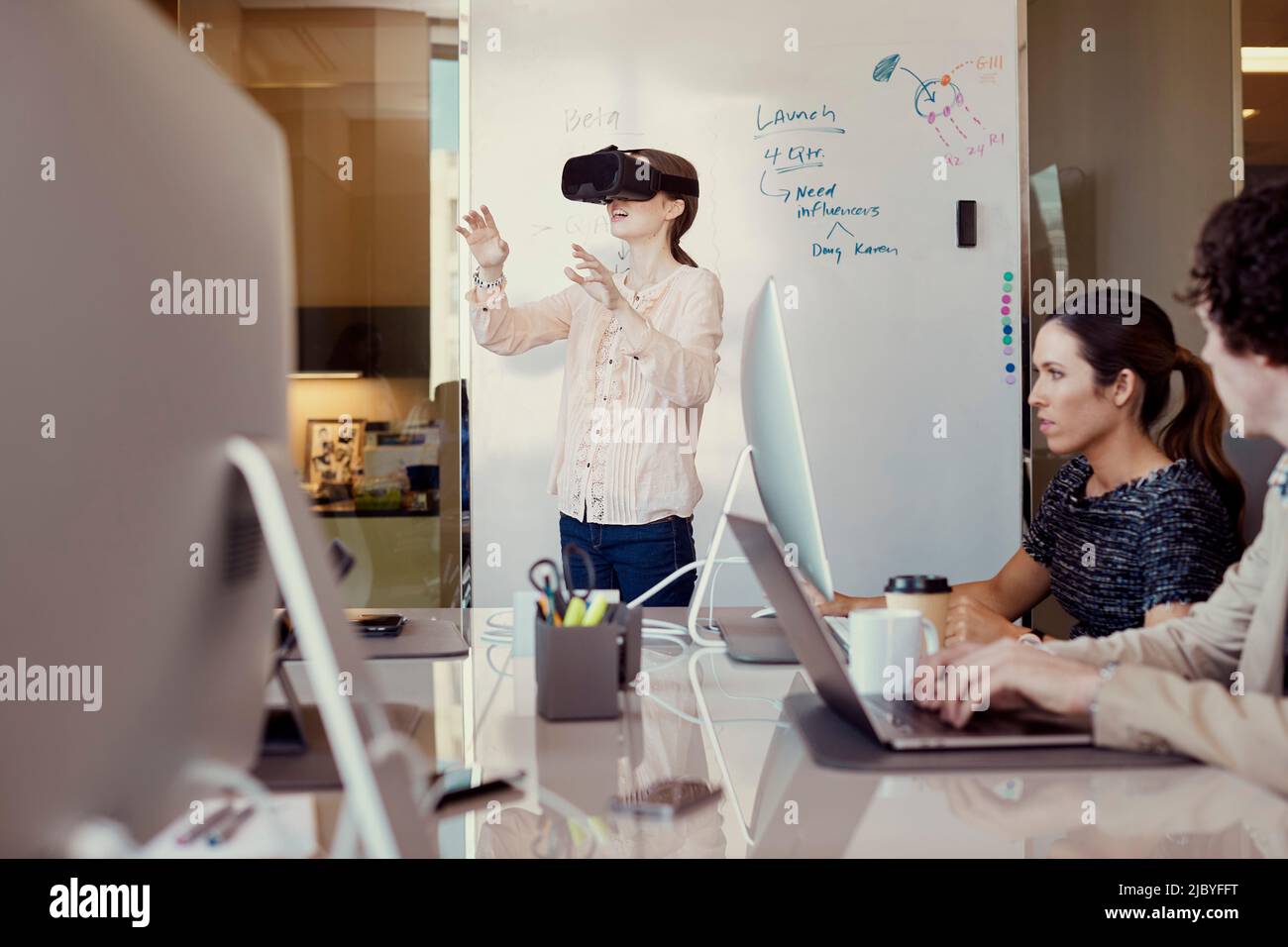 -Arbeiter arbeiten am Computer im Büro, während Frau mit Virtual Reality Headset steht vor dem trocken löschen Board mit Flussdiagramm im Hintergrund Stockfoto