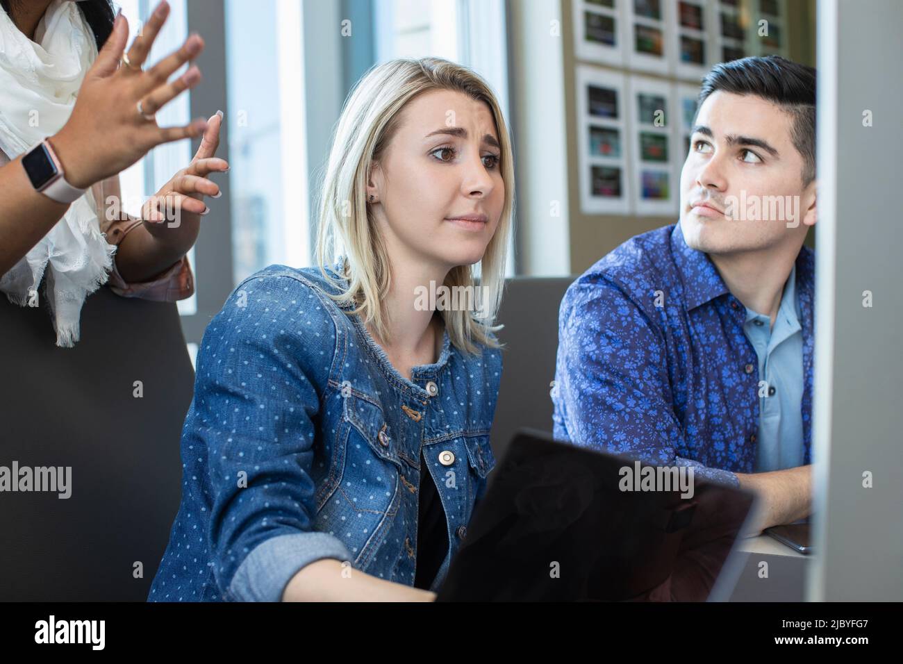Junge Frau, die im Büro einen Computer benutzt und Kollegen etwas auf ihrem Bildschirm zeigt Stockfoto