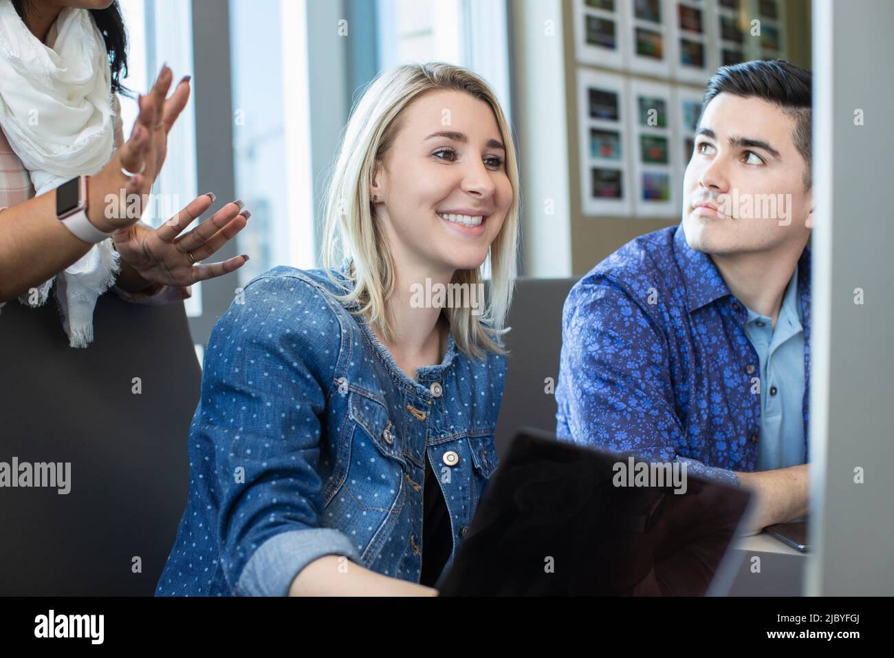 Junge Frau, die im Büro einen Computer benutzt und Kollegen etwas auf ihrem Bildschirm zeigt Stockfoto