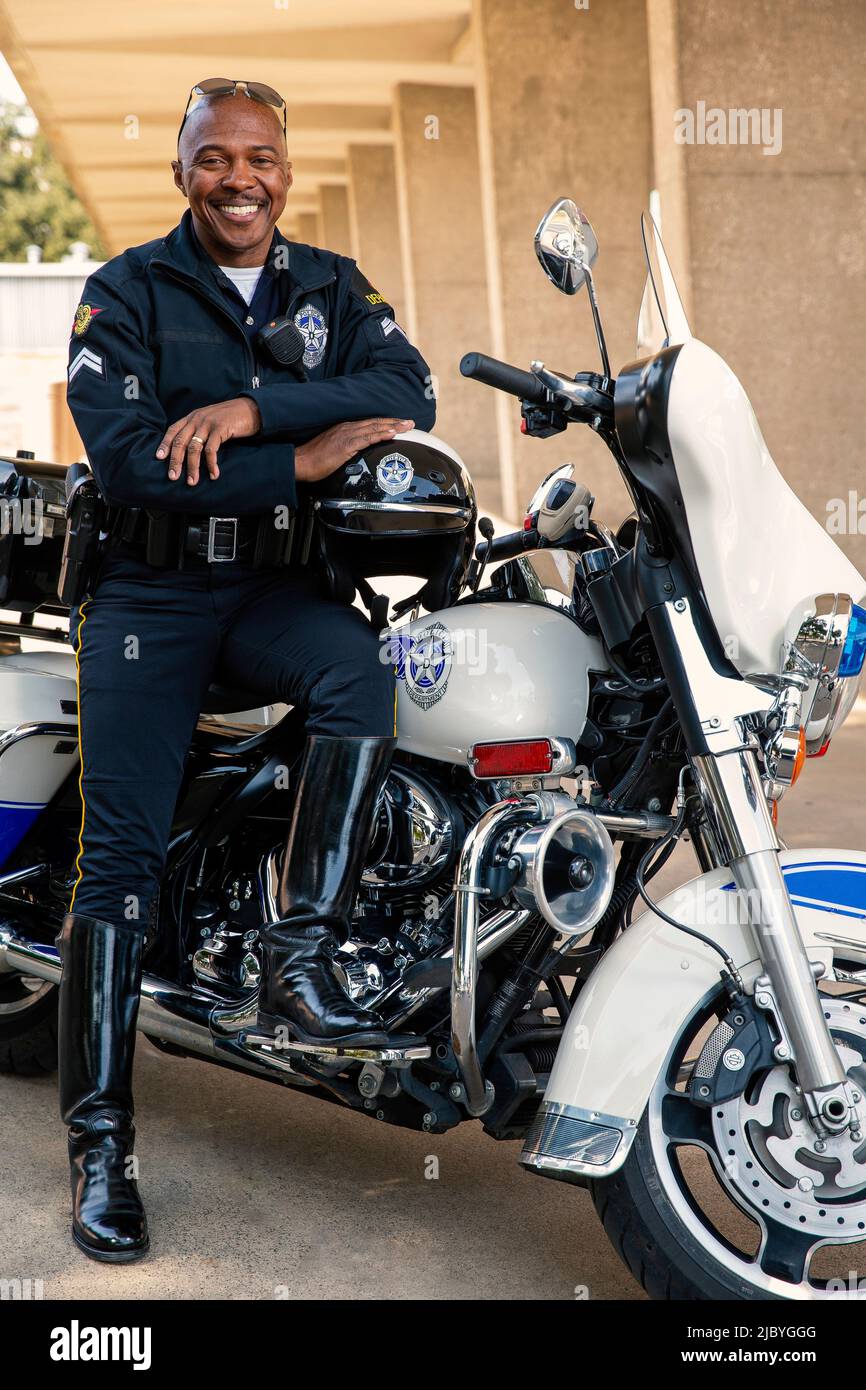 Porträt eines Polizisten, der draußen auf seinem Motorrad sitzt und lächelnd auf die Kamera blickt Stockfoto
