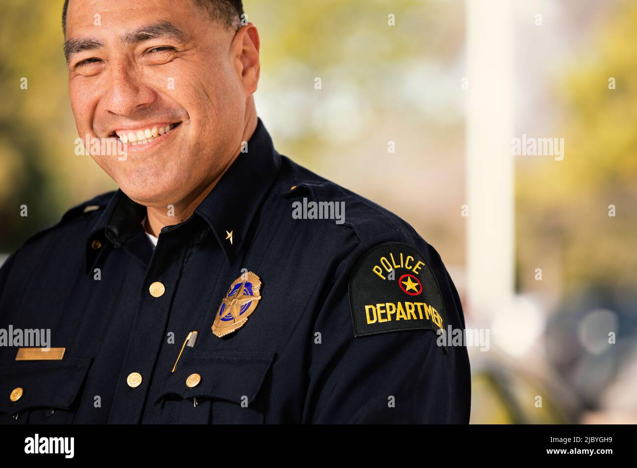 Porträt eines Polizisten, der draußen mit gekreuzten Armen steht und lächelnd auf die Kamera blickt Stockfoto