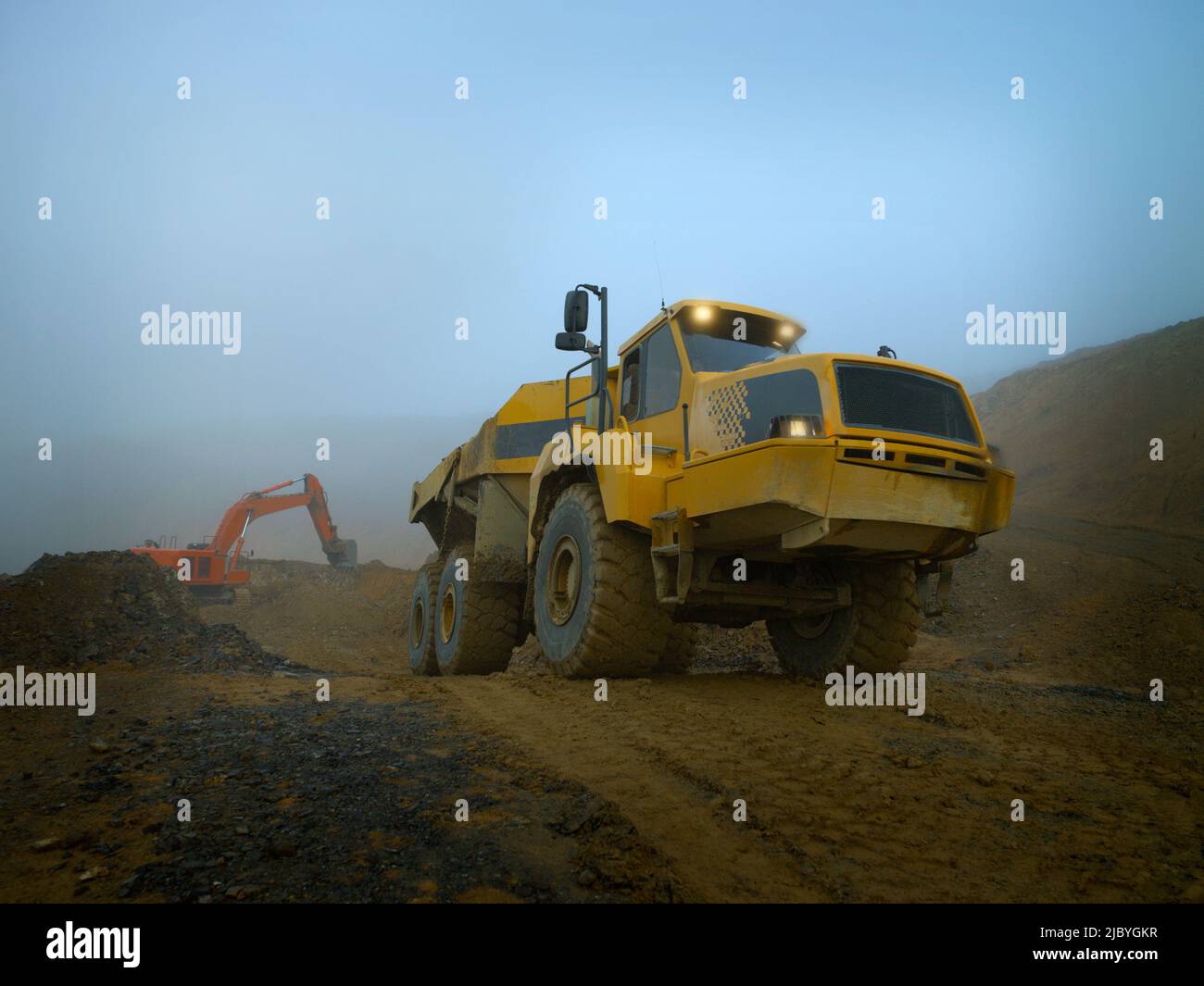 Erdbewegungsfahrzeug mit Beleuchtung und Bagger im nebligen Steinbruch Stockfoto