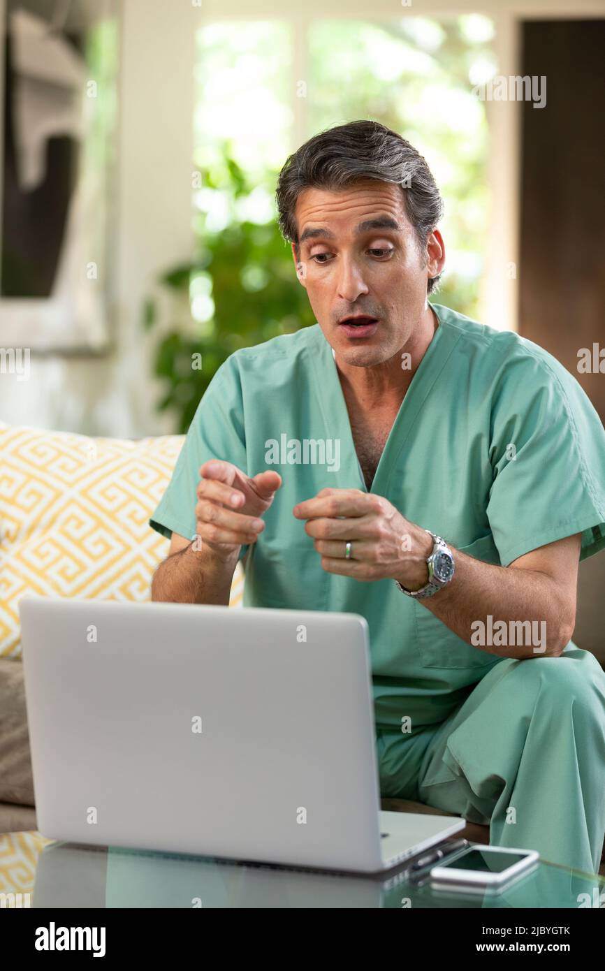 Hispanischer Arzt, der von zu Hause aus Telemedizin praktiziert, mit einem Laptop-Computer, um den Patienten bei einem Videoanruf zu konsultieren Stockfoto