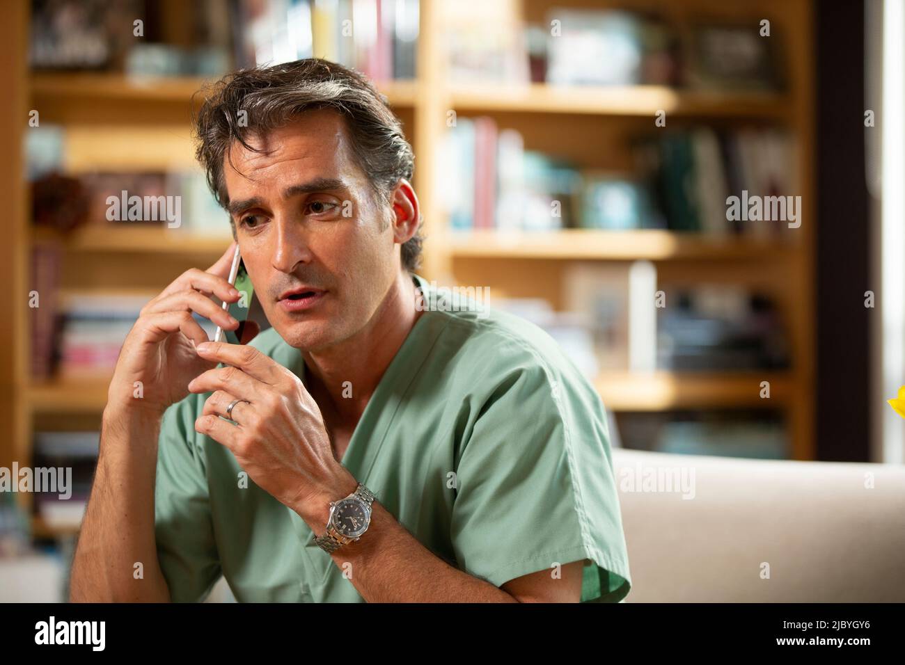 Hispanischer Arzt, der in seinem Büro Telemedizin praktiziert und mit dem Patienten am Handy spricht Stockfoto