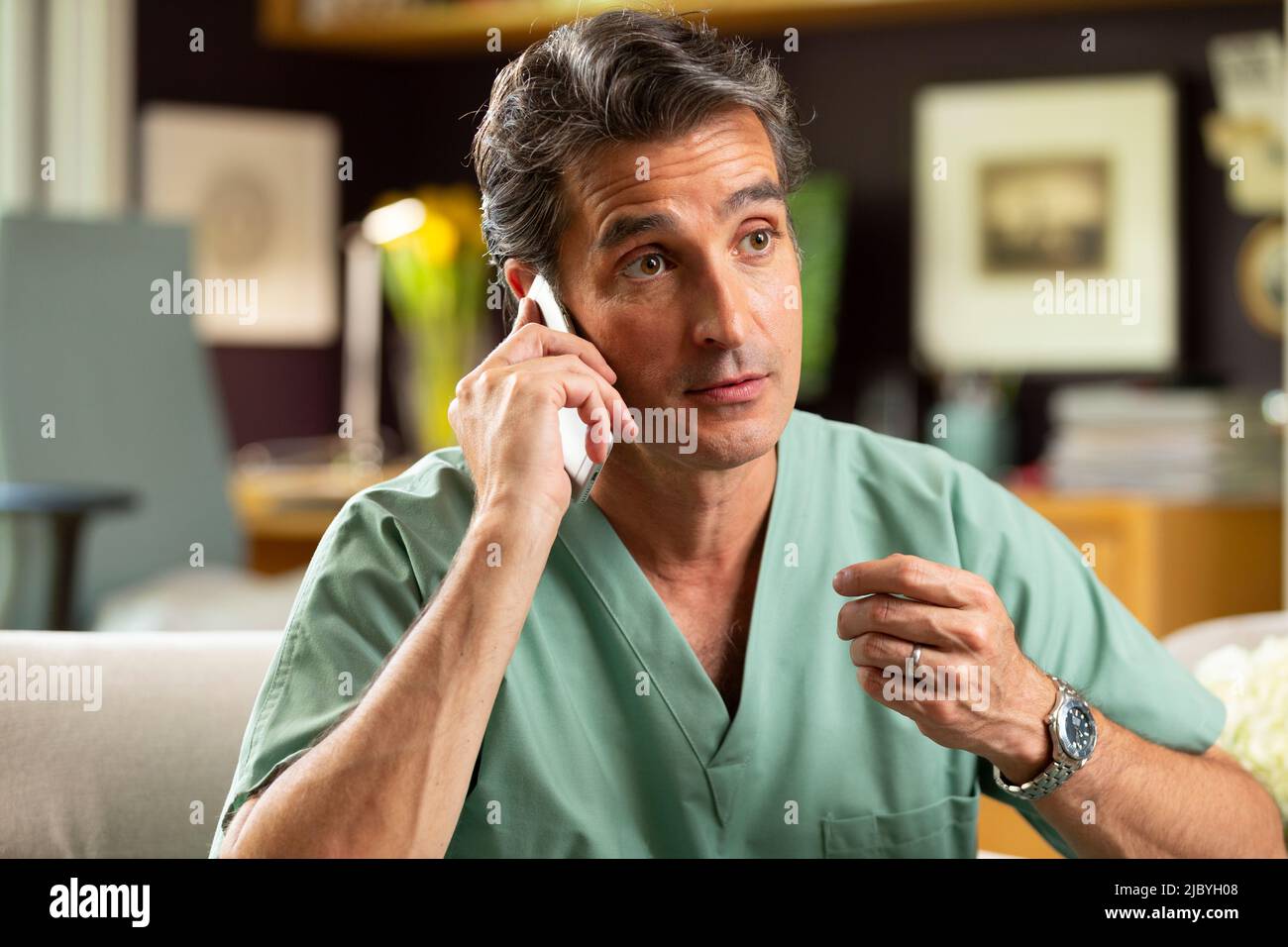 Hispanischer Arzt, der in seinem Büro Telemedizin praktiziert und mit dem Patienten am Handy spricht Stockfoto