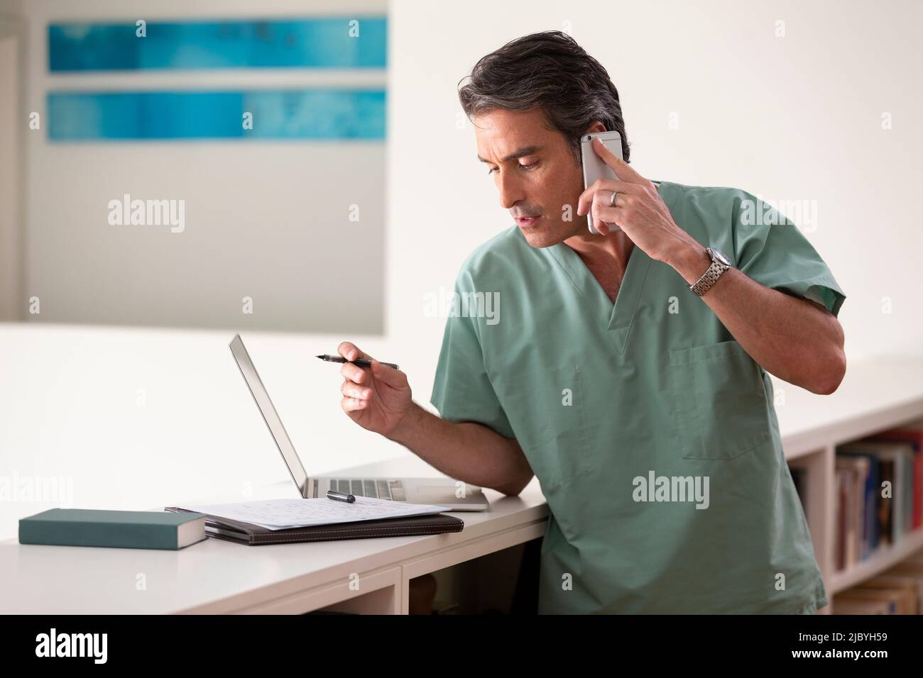 Hispanischer Arzt in seinem Haus, der Telemedizin praktiziert, am Handy telefoniert und Notizen macht Stockfoto