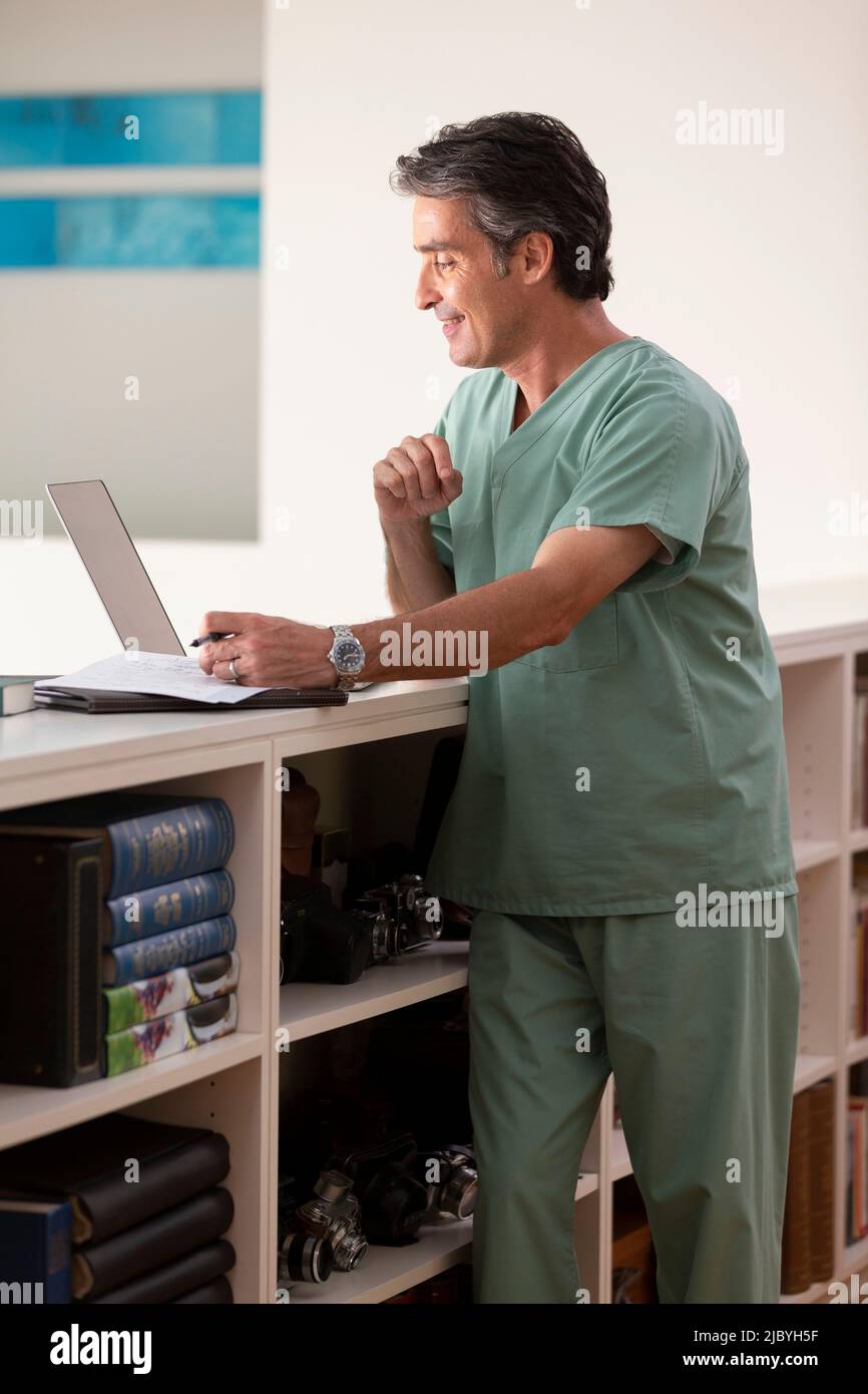 Hispanischer männlicher Arzt in seinem Haus, der Telemedizin praktiziert und eine Videokonferenz auf dem Laptop hat Stockfoto