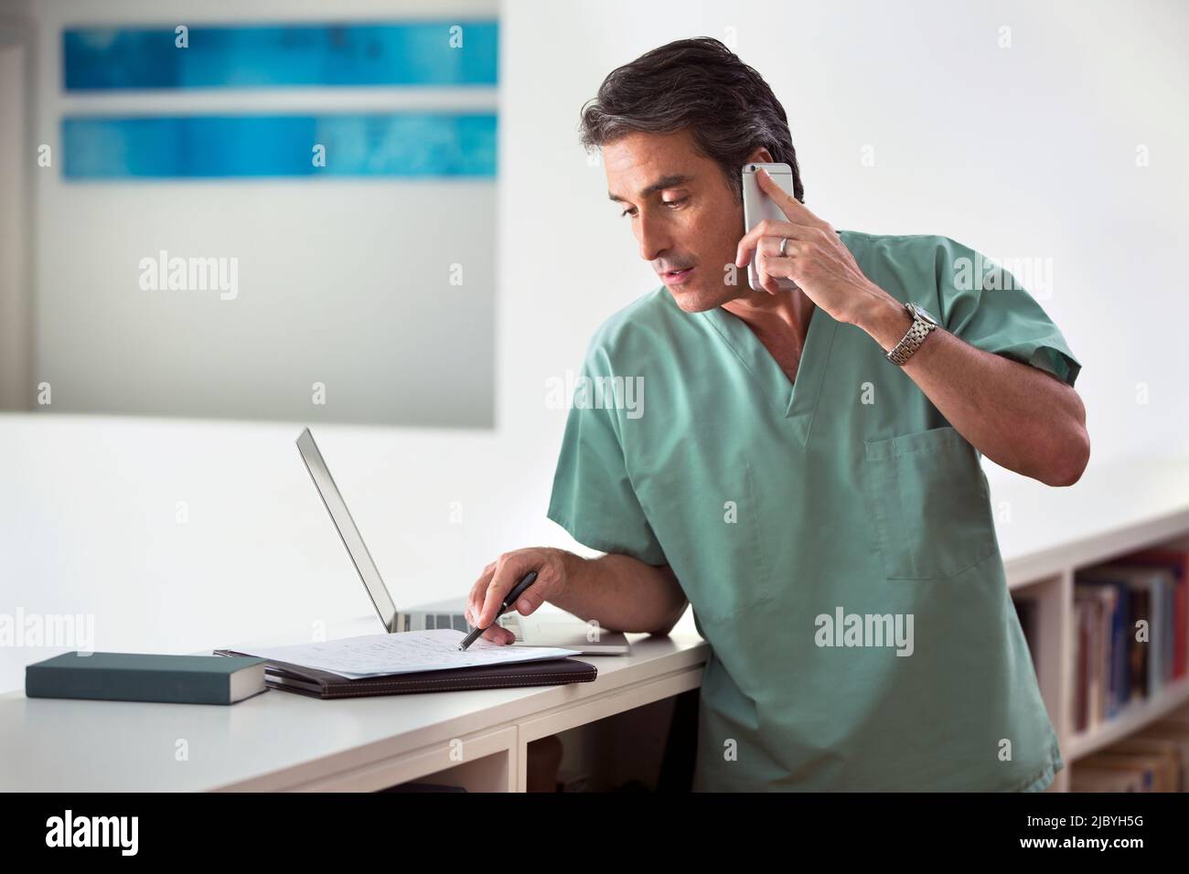 Hispanischer Arzt in seinem Haus, der Telemedizin praktiziert, am Handy telefoniert und Notizen macht Stockfoto