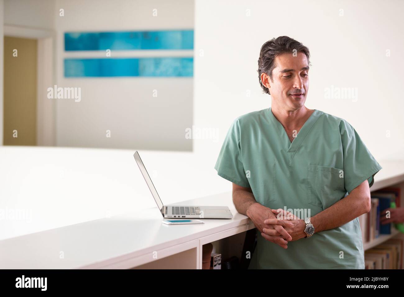 Porträt eines hispanischen männlichen Arztes in seinem Haus, der eine Pause vom Praktizieren der Telemedizin macht und von der Kamera schaut Stockfoto