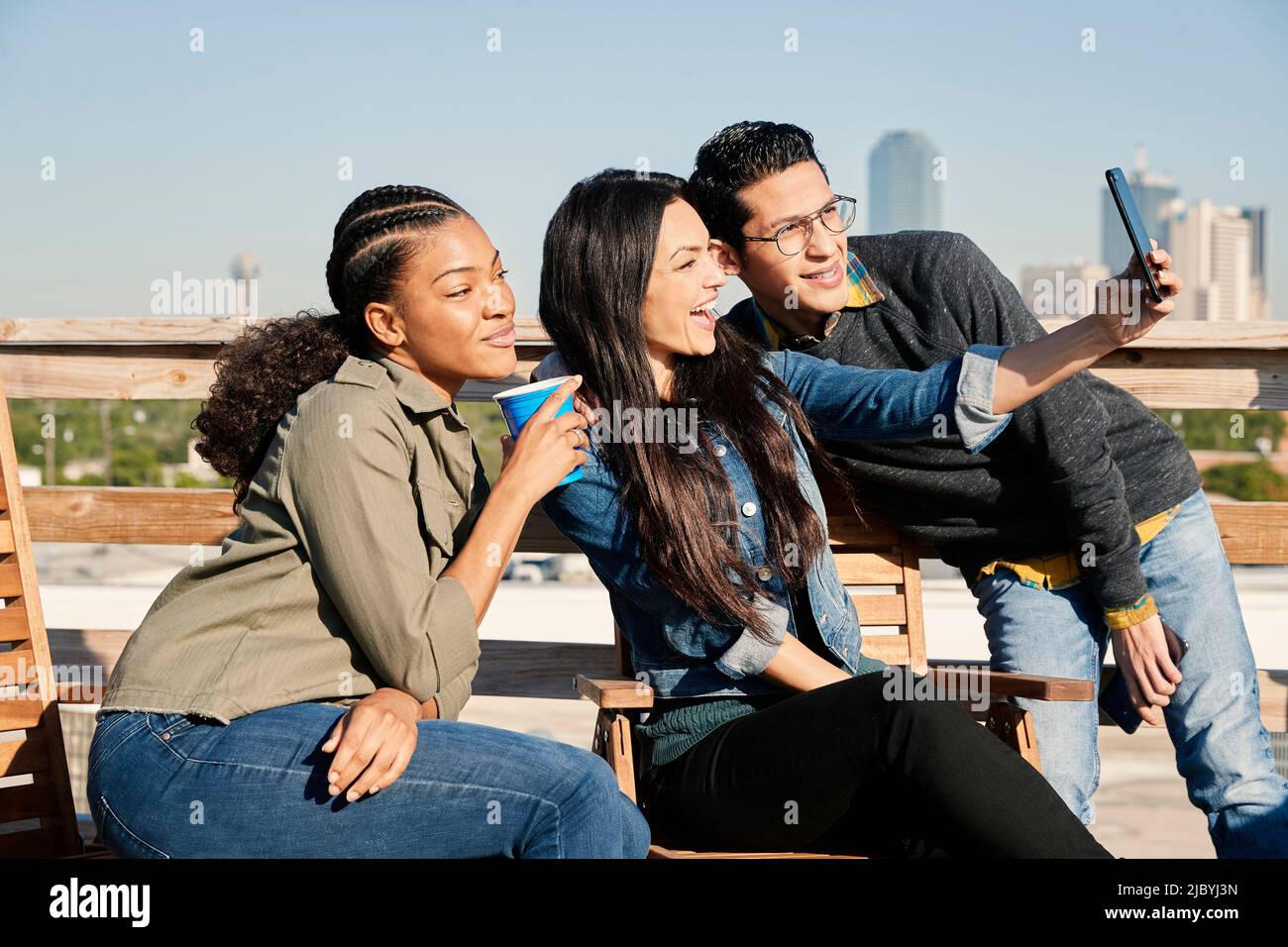 Eine Gruppe junger Mitarbeiter, die auf der Dachterrasse herumhängen, zwei Frauen und ein Mann, die Selfie mit dem Mobiltelefon machen Stockfoto