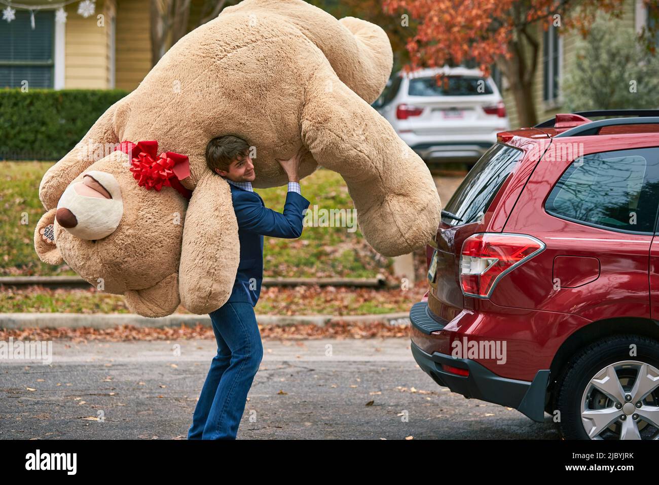 Breiter Schuss eines Mannes, der einen überdimensionalen Teddybären über seine Schulter hält. Stockfoto