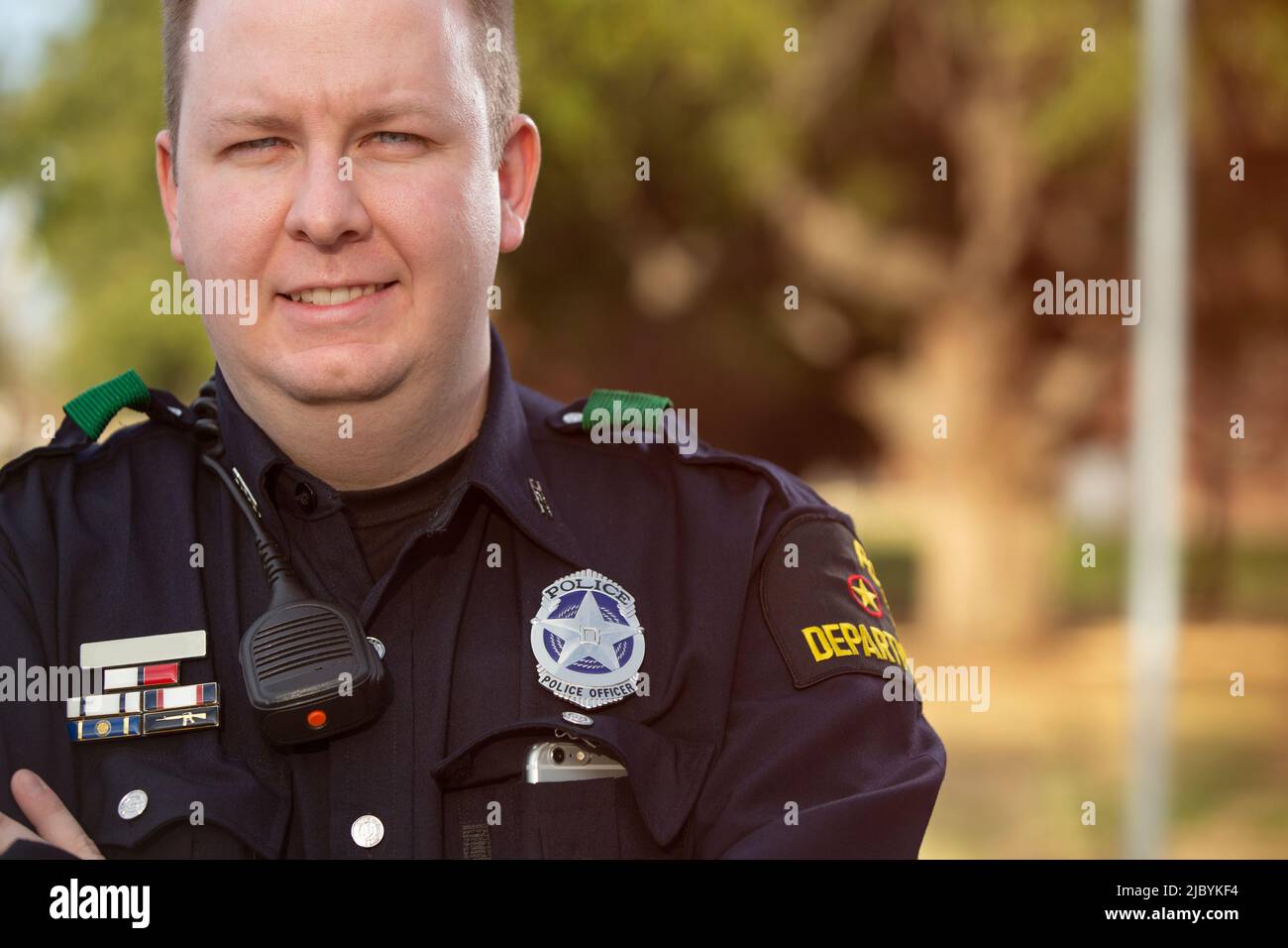 Porträt eines Polizisten, der draußen mit gekreuzten Armen steht und lächelnd auf die Kamera blickt Stockfoto