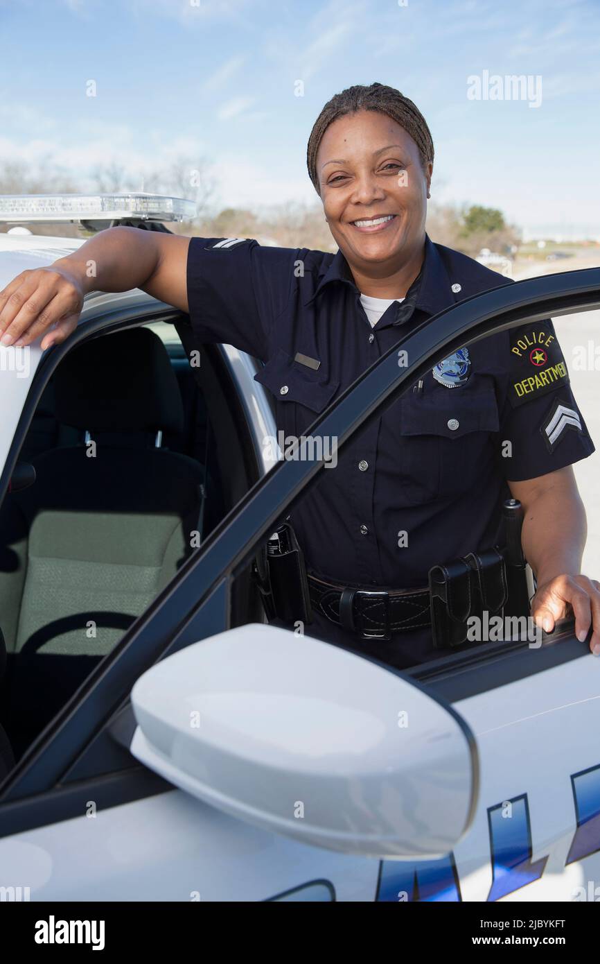Polizistin, die in der Tür des Polizeiwagens steht und lächelnd auf die Kamera schaut Stockfoto