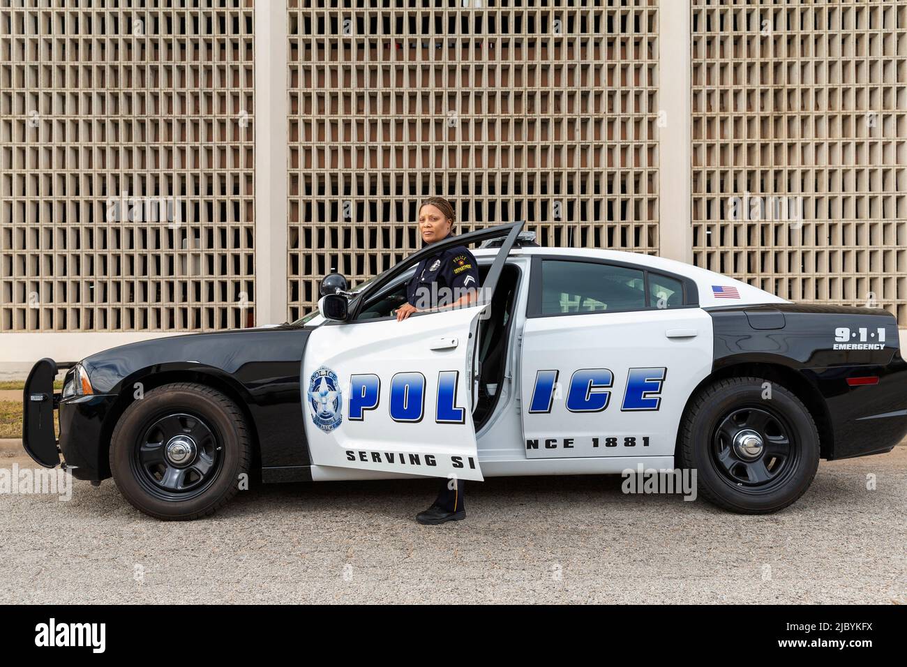 Polizistin, die in der Tür des Polizeiwagens steht und auf die Kamera schaut Stockfoto