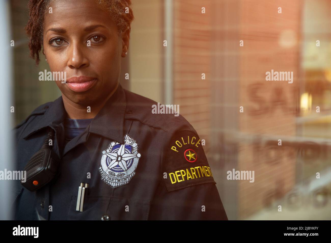 Porträt einer Polizeifrau, die vor einem großen Glasfenster steht, mit Reflexionen, die auf die Kamera schauen Stockfoto