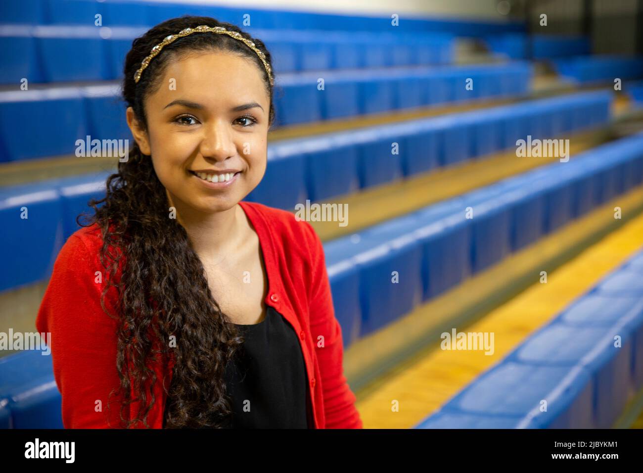 Lächelndes Porträt einer jungen ethnischen Frau, die auf Tribünen in der Turnhalle sitzt Stockfoto