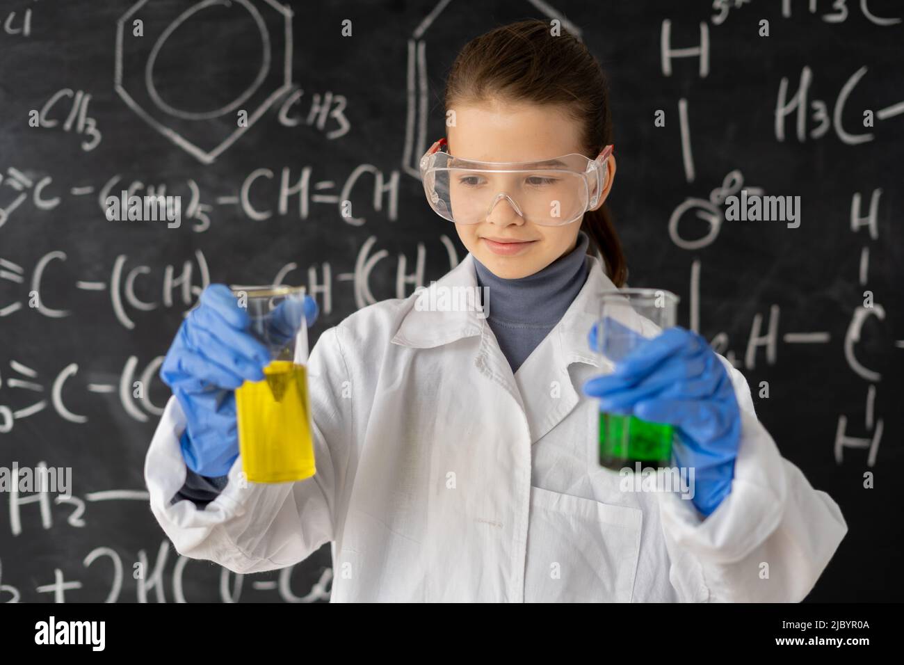 Lustige Wissenschaftler Kind mit Brille im Labormantel mit chemischen Kolben, Tafel Hintergrund mit Wissenschaft Formeln im Labor, zurück zur Schule Stockfoto