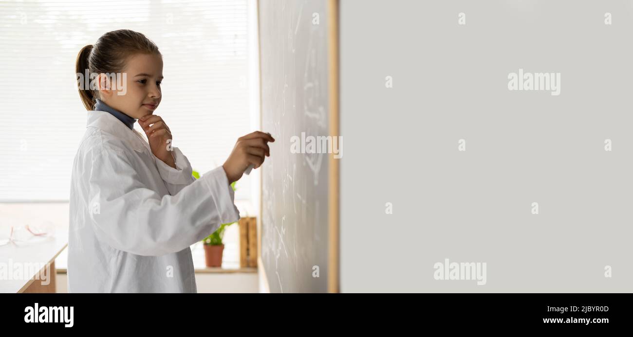 Nachdenkliches Schulmädchen schreibt Formeln bei einer Chemiestunde in der Nähe der Tafel Stockfoto