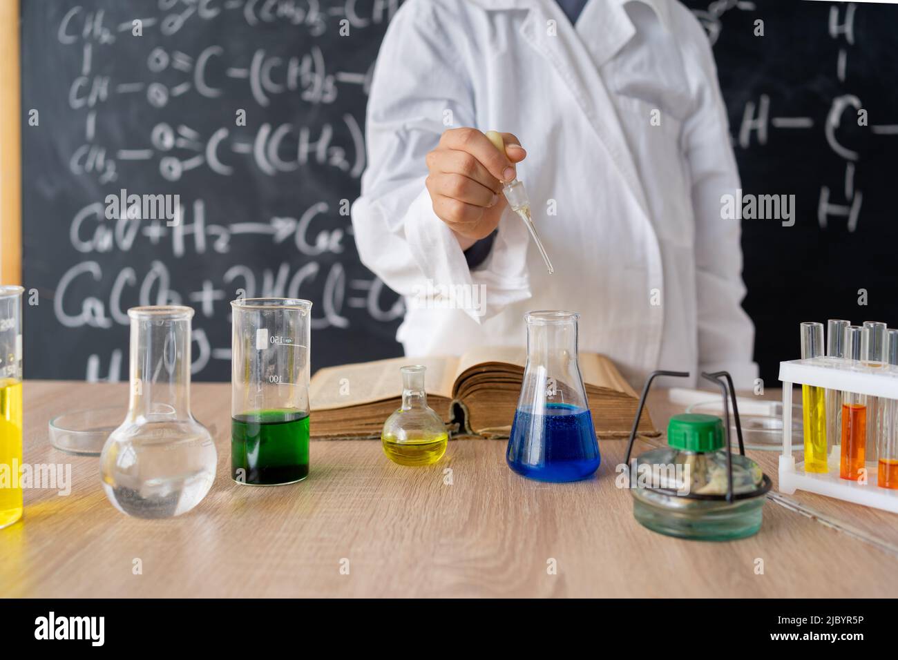 Studentin, die Forschung lernt und ein chemisches Experiment durchführt, während sie im Science-Class-Kurs die Analyse und das Mischen von Flüssigkeit in Glas auf den Tisch stellt Stockfoto