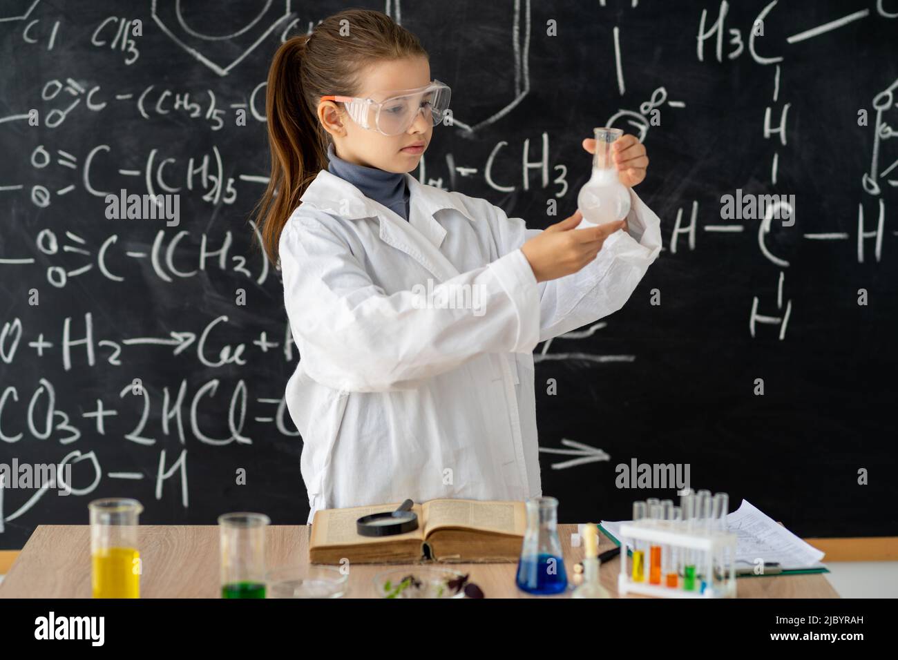 Schülerin im weißen Mantel, die im Chemielabor Experimente mit Flüssigkeiten macht, macht Mädchen in einer Chemiestunde ein chemisches Experiment Stockfoto