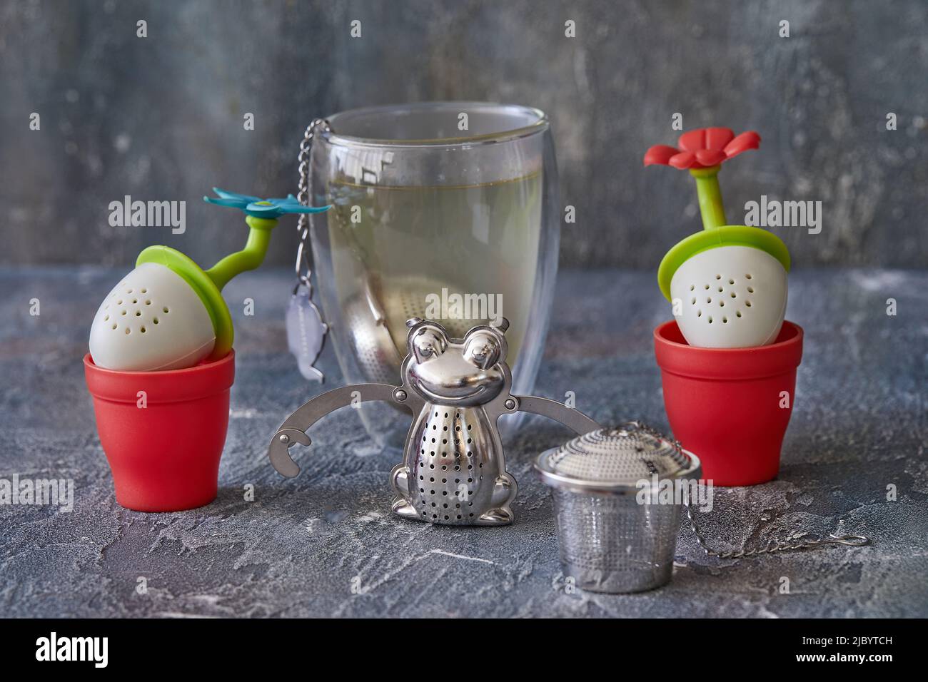 Tee-Brauwerkzeuge in Form von Fröschen und Blumen mit einem Glas Tee. Stockfoto
