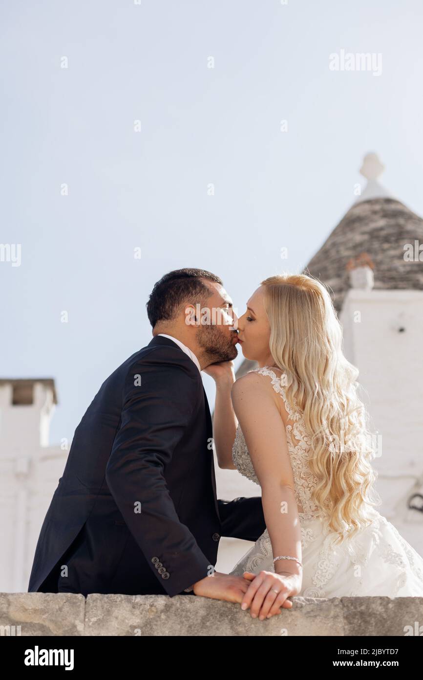 Vertikale Nahaufnahme verheiratetes Paar, hübsche blonde Frau, Braut und dunkelhaariger bärtiger Mann, Bräutigam küssen sich im Freien zusammen Stockfoto