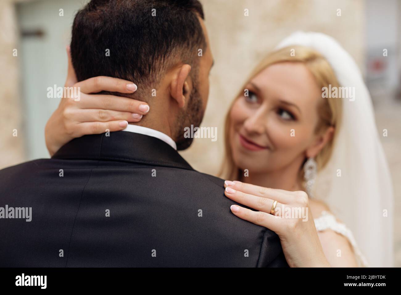 Romantisches Paar, einander anblickend, Braut hält Bräutigam Gesicht in den Händen mit Maniküre und goldenem Ring. Modisch Stockfoto