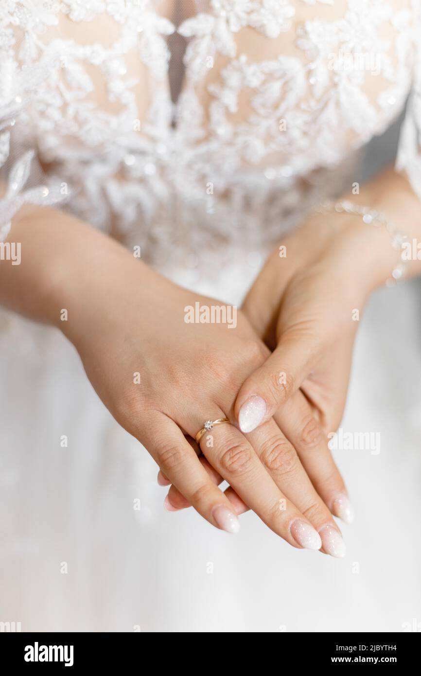 Nahaufnahme Foto von eleganten, glänzenden sanften Frau Hände halten einander, Braut mit ausgezeichneter Maniküre. Weißes Hochzeitskleid Stockfoto