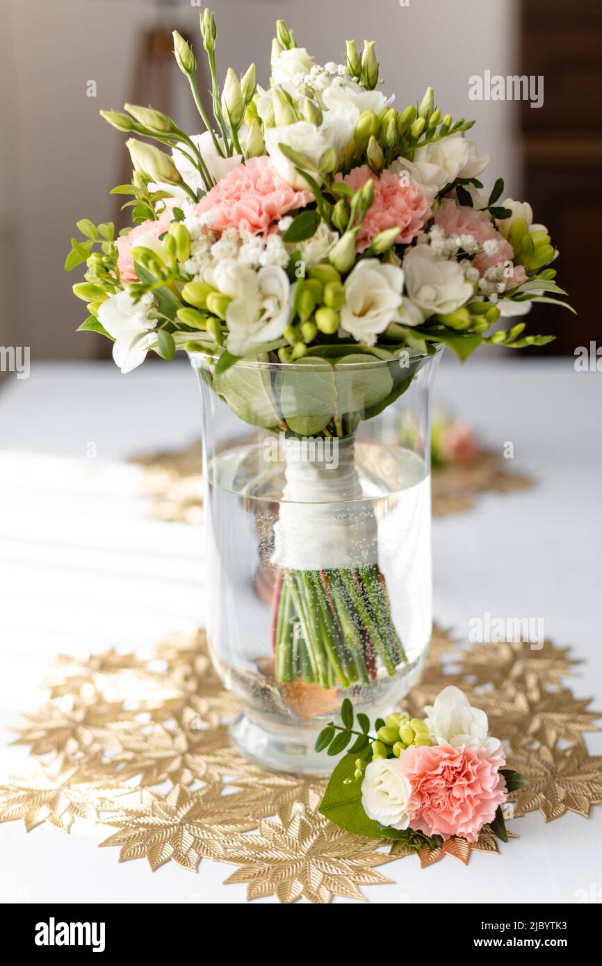 Vertikal aus frischem Blumenstrauß in transparenter Wasservase auf Tisch mit bedruckter Tischdecke. Blumenarrangement für Hochzeiten Stockfoto